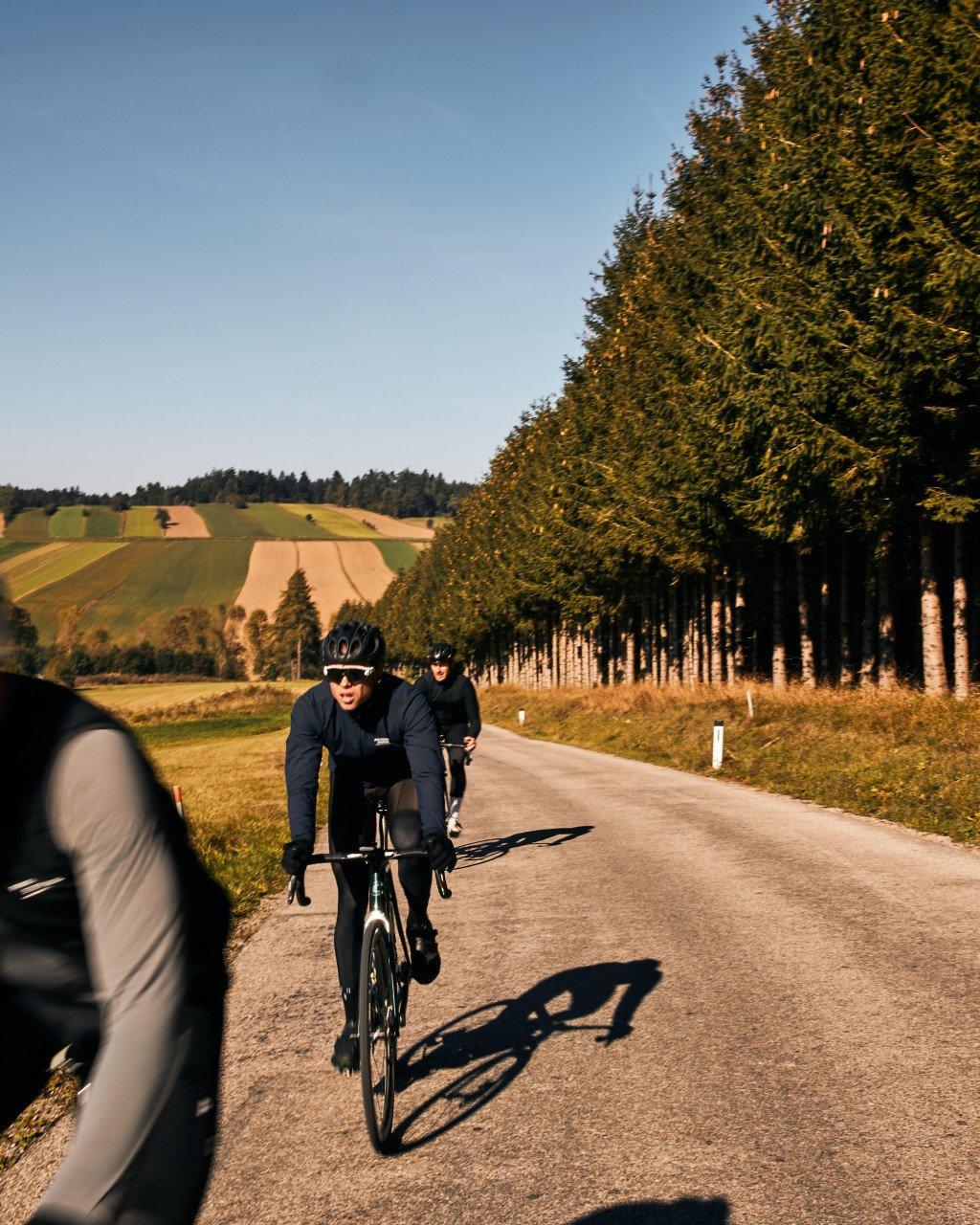 Cyclists in black time trial gear racing on rural road through countryside landscape