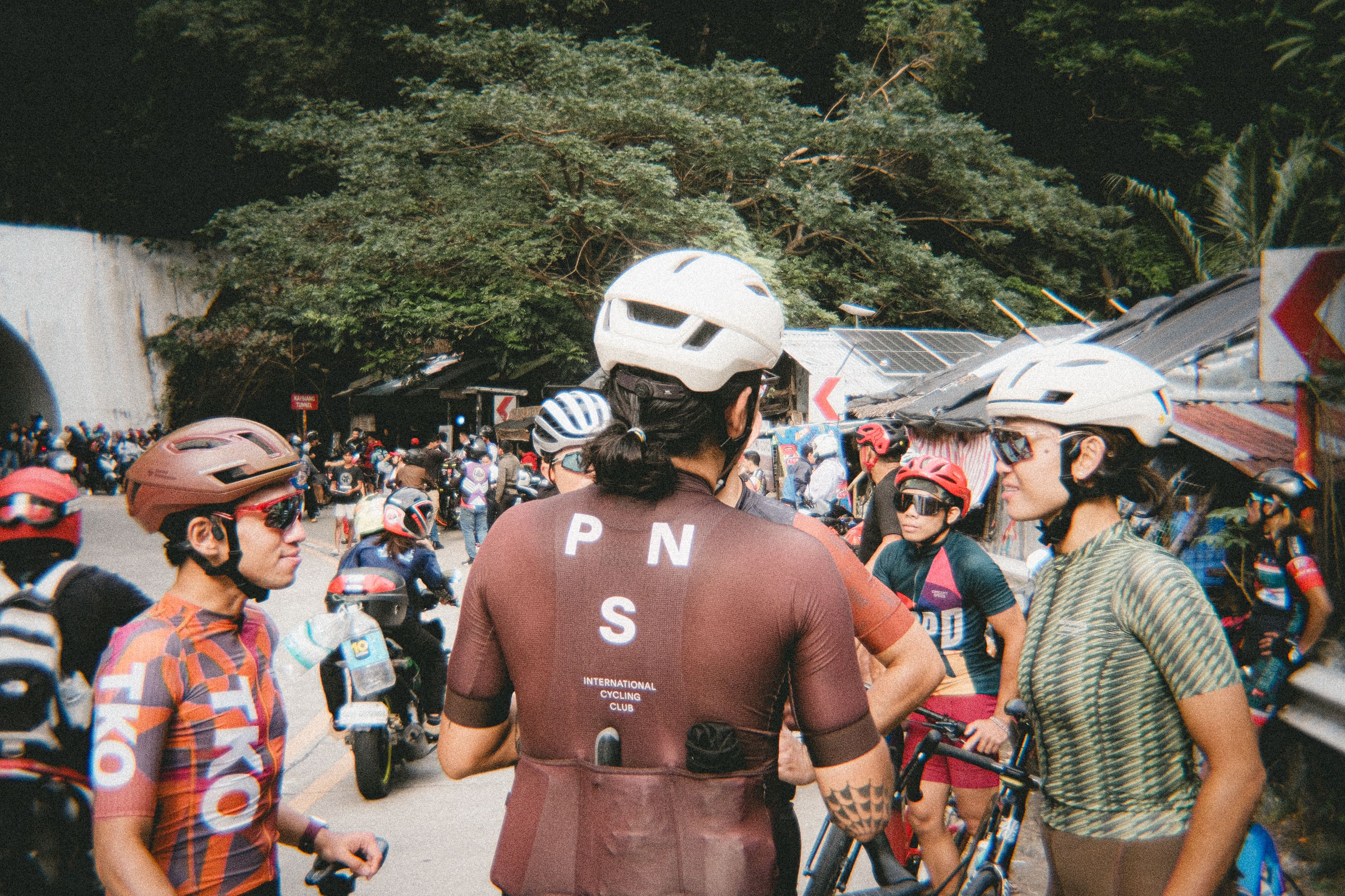 Cyclists gathering at event, central rider wearing burgundy jersey with back logo and "International Cycling Club" text