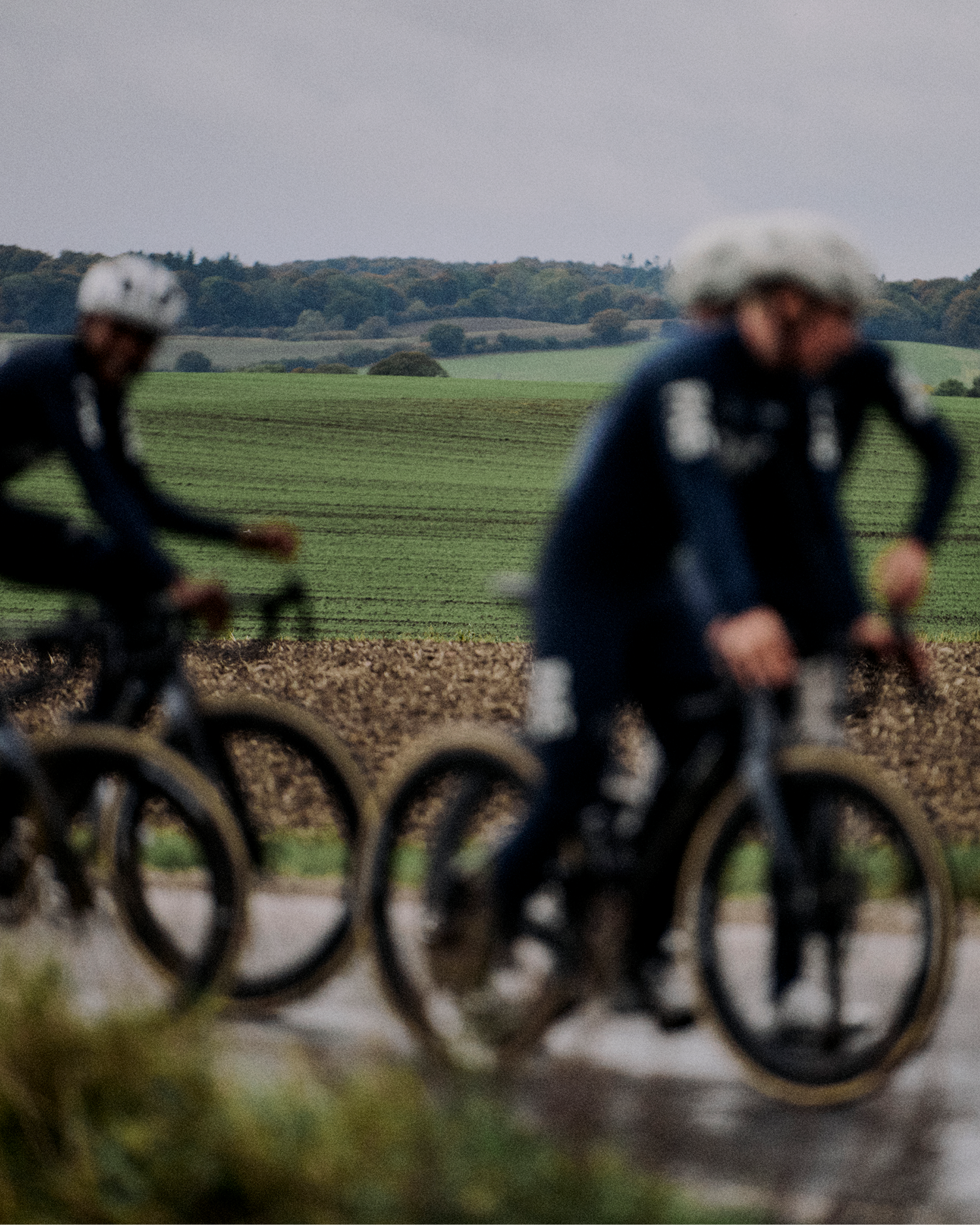Two cyclists in dark winter cycling apparel riding through rural countryside with rolling hills