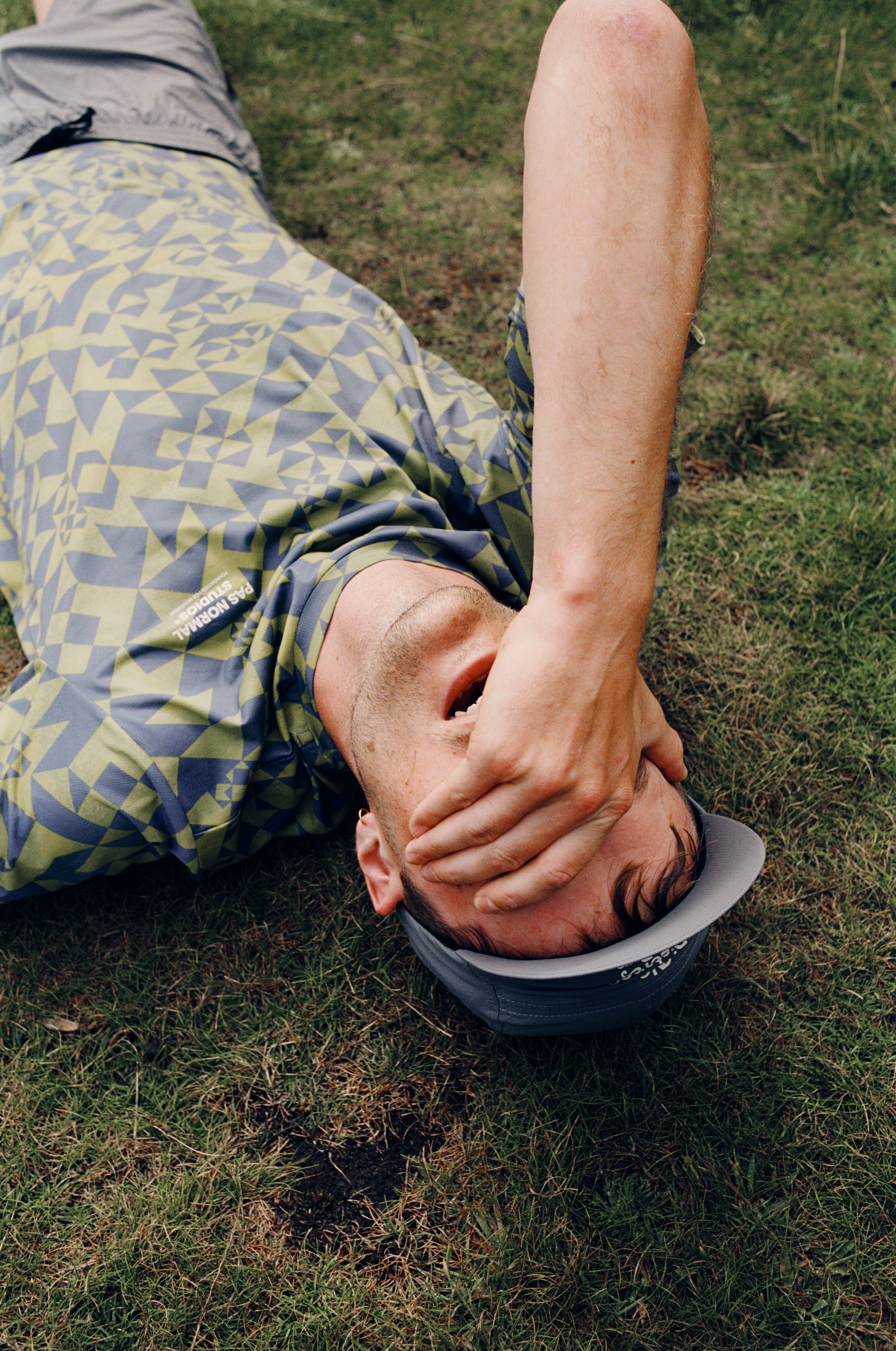 Model lying on grass wearing yellow geometric print cycling jersey, hand covering face