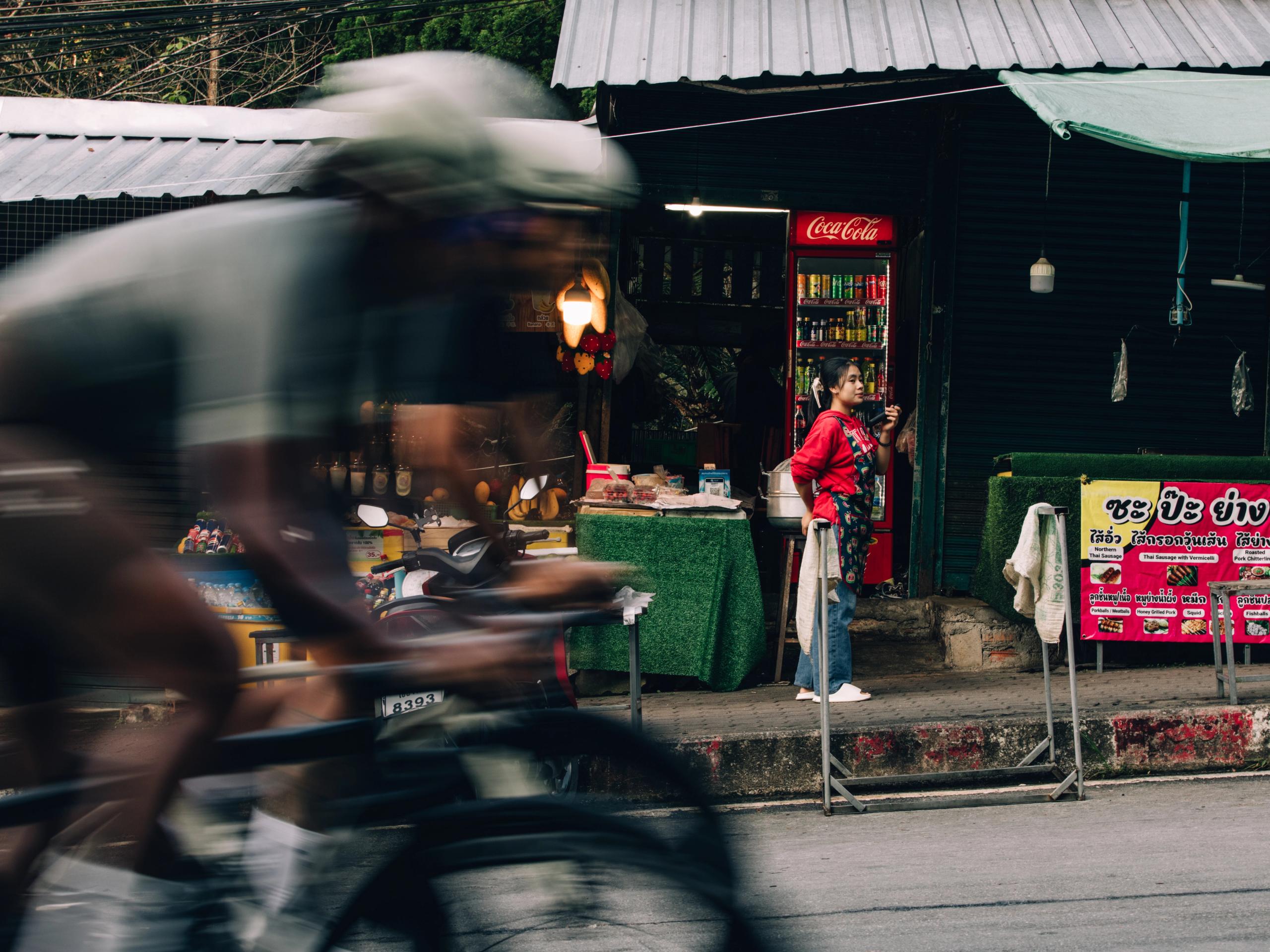 Cyclist in motion blur passing street food vendor in urban setting