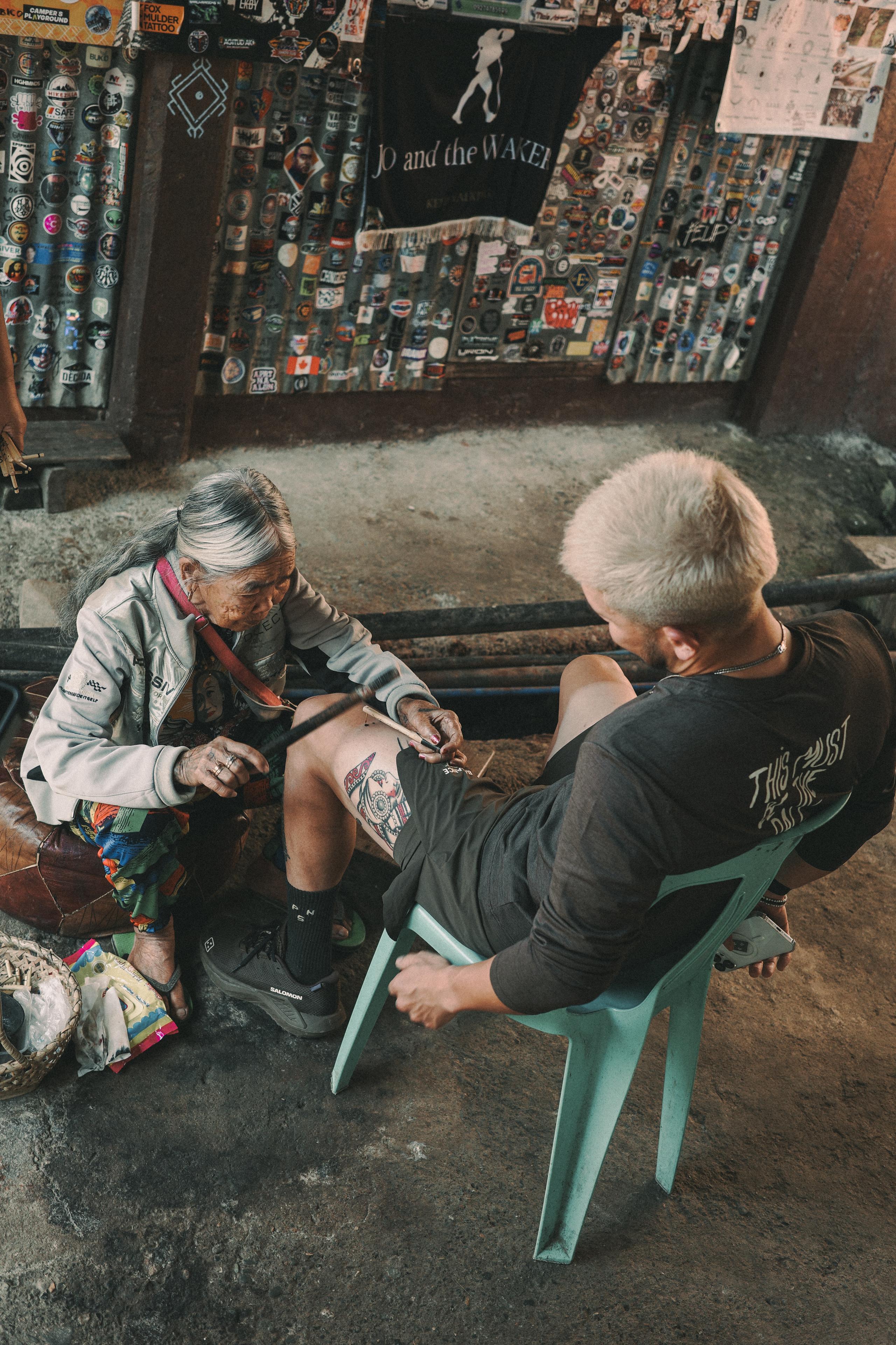 Model getting tattoo in shop wearing dark long-sleeve cycling jersey with logo