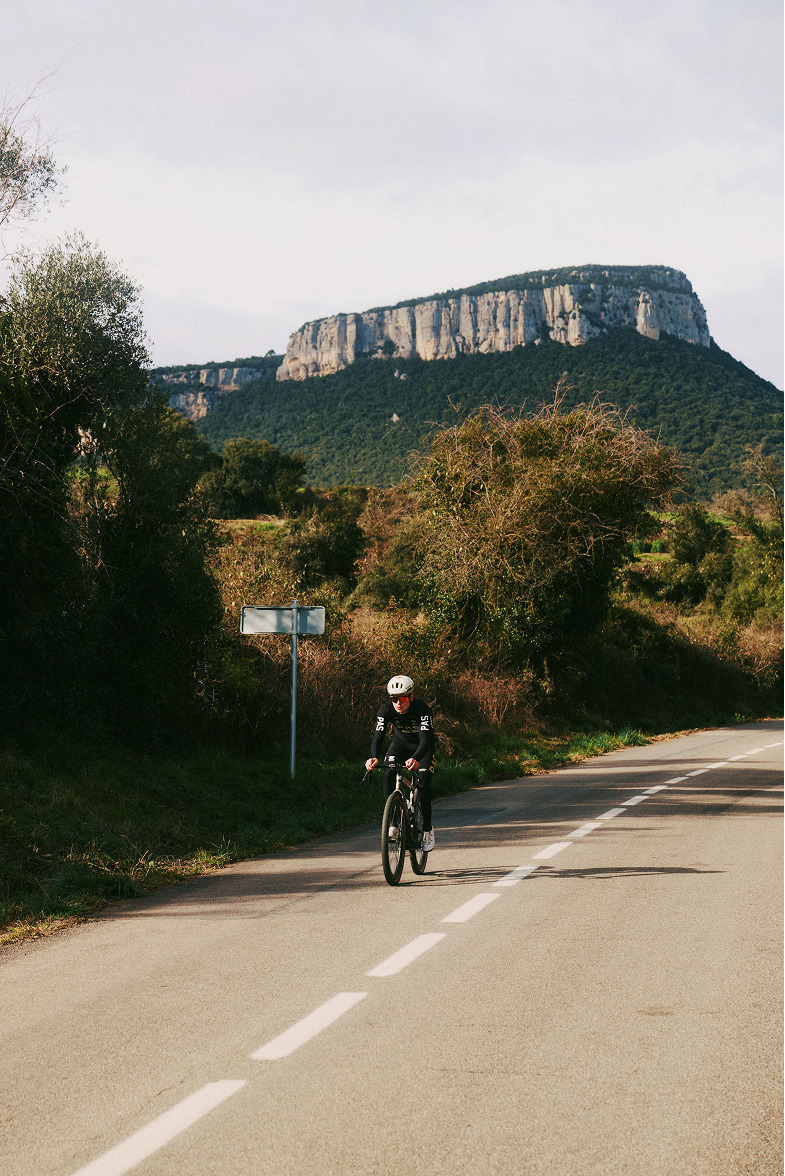 Model wearing black cycling kit on time trial bike on countryside road with mountain backdrop
