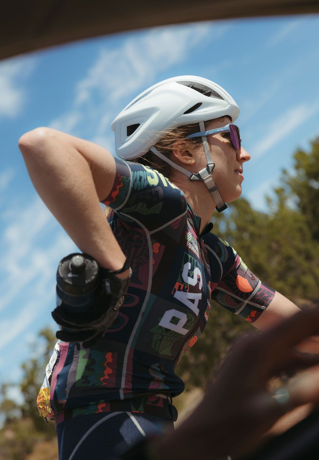 Model wearing PAS collection cycling jersey with colorful botanical print and white helmet outdoors