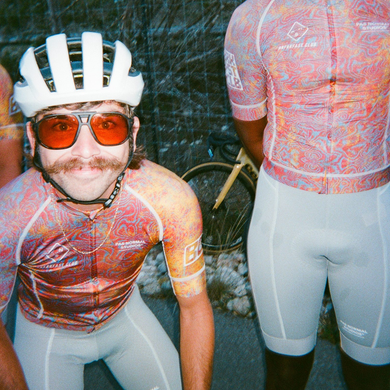 Models wearing colorful patterned jerseys and white cycling shorts from Breakfast Club collaboration