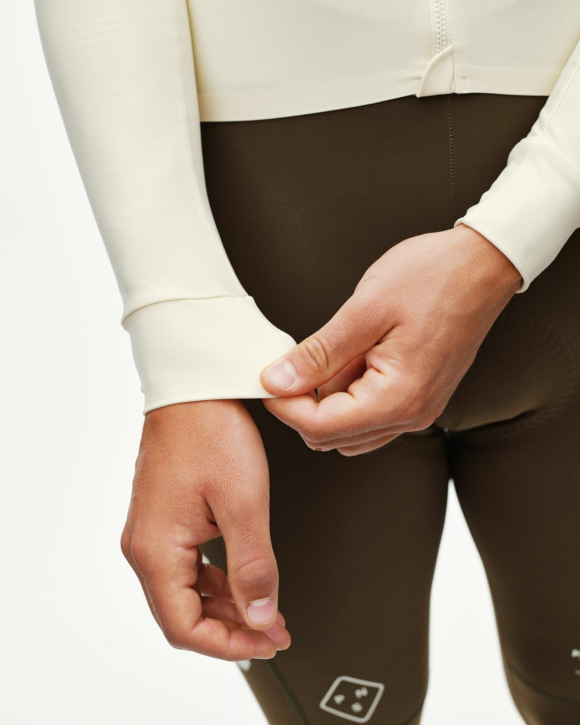 Sand PAS Mechanism long sleeve cycling jersey, detail view on model showing ribbed cuff with dark olive bib tights