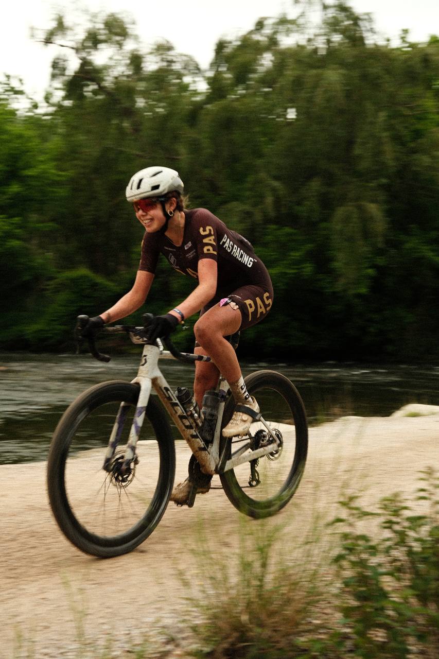 Model wearing brown cycling jersey and shorts with yellow lettering on time trial bike in motion