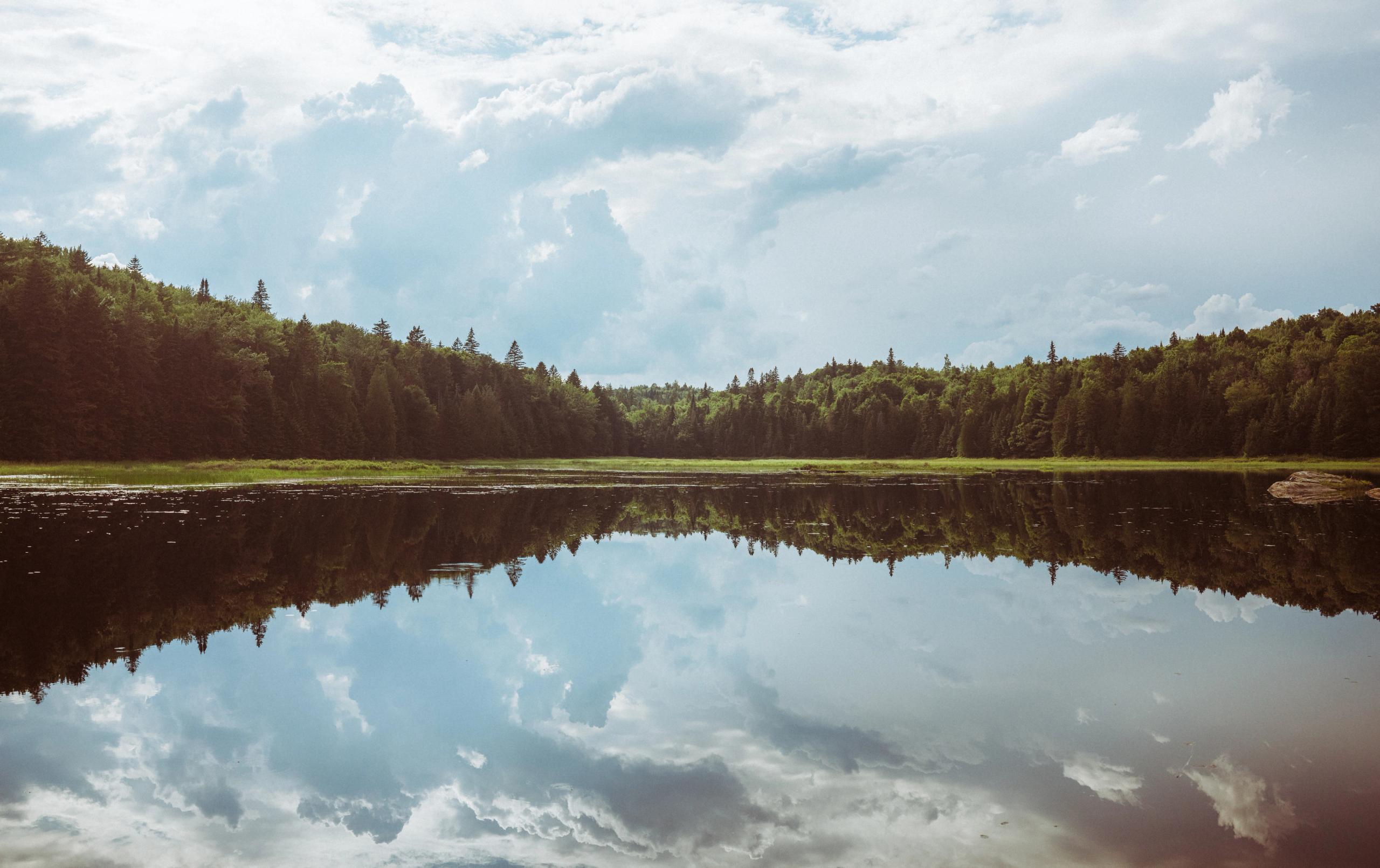 Serene lake reflecting cloudy sky surrounded by forested hills