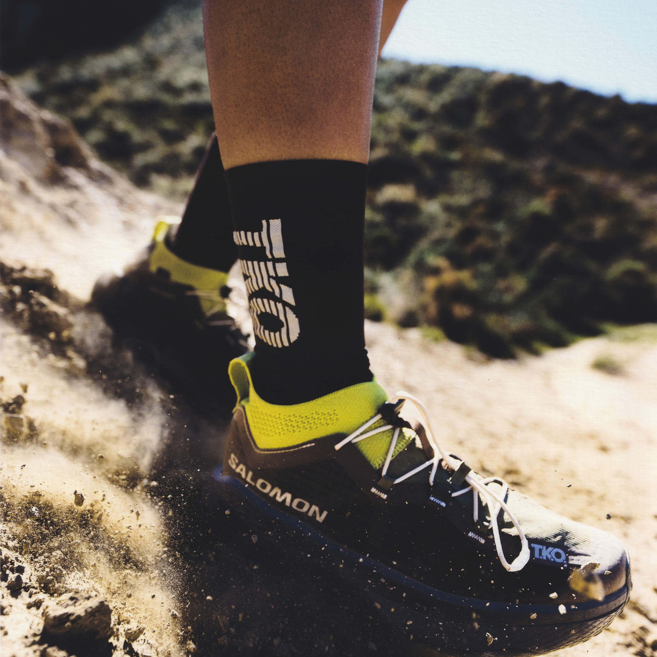 Black sock with logo worn with Salomon running shoe on trail terrain