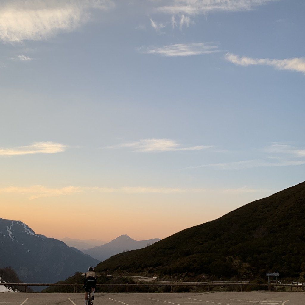 Cyclist on mountain road at sunset with alpine peaks in background