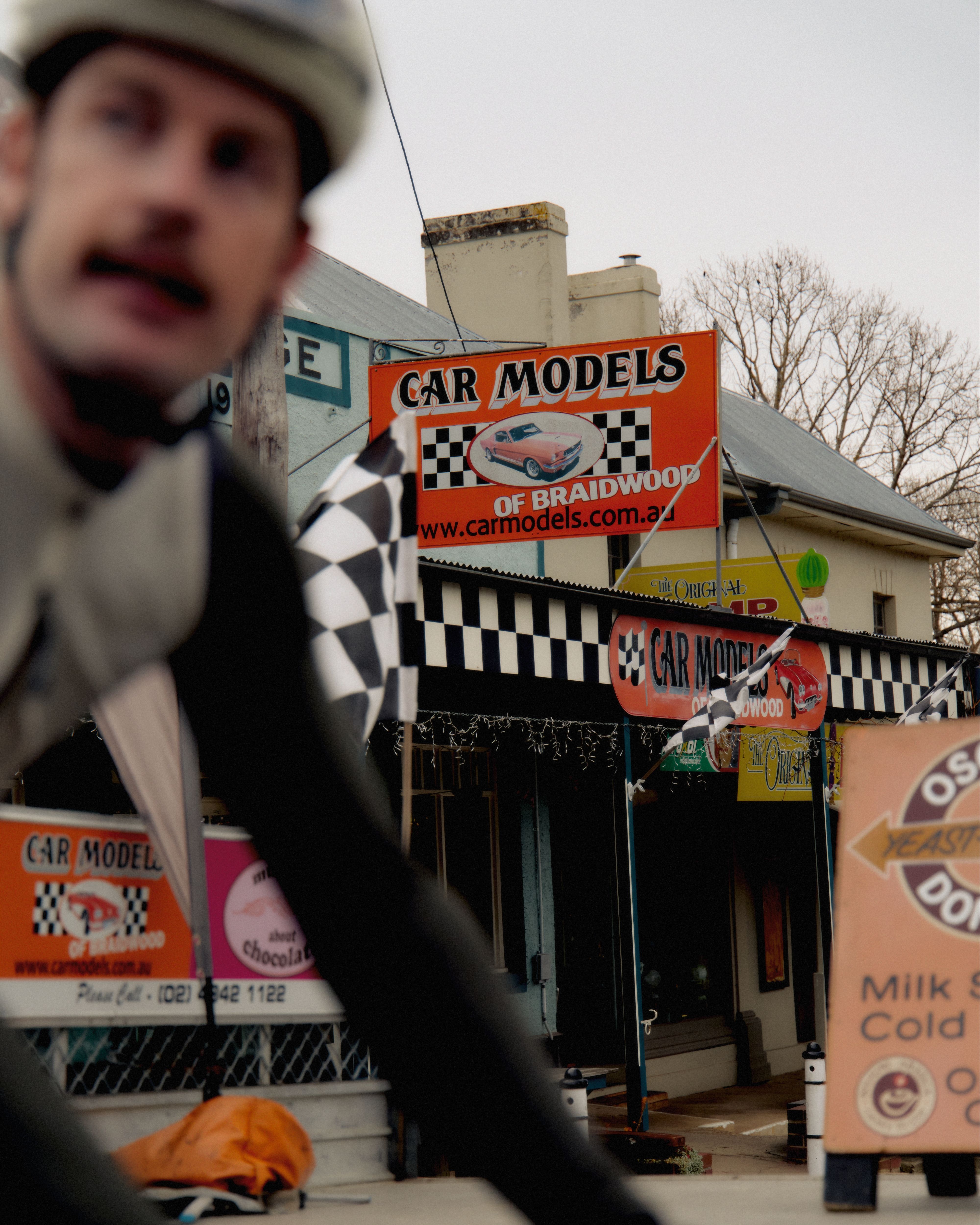 Model wearing white cycling cap with checkered flag pattern in front of car model shop