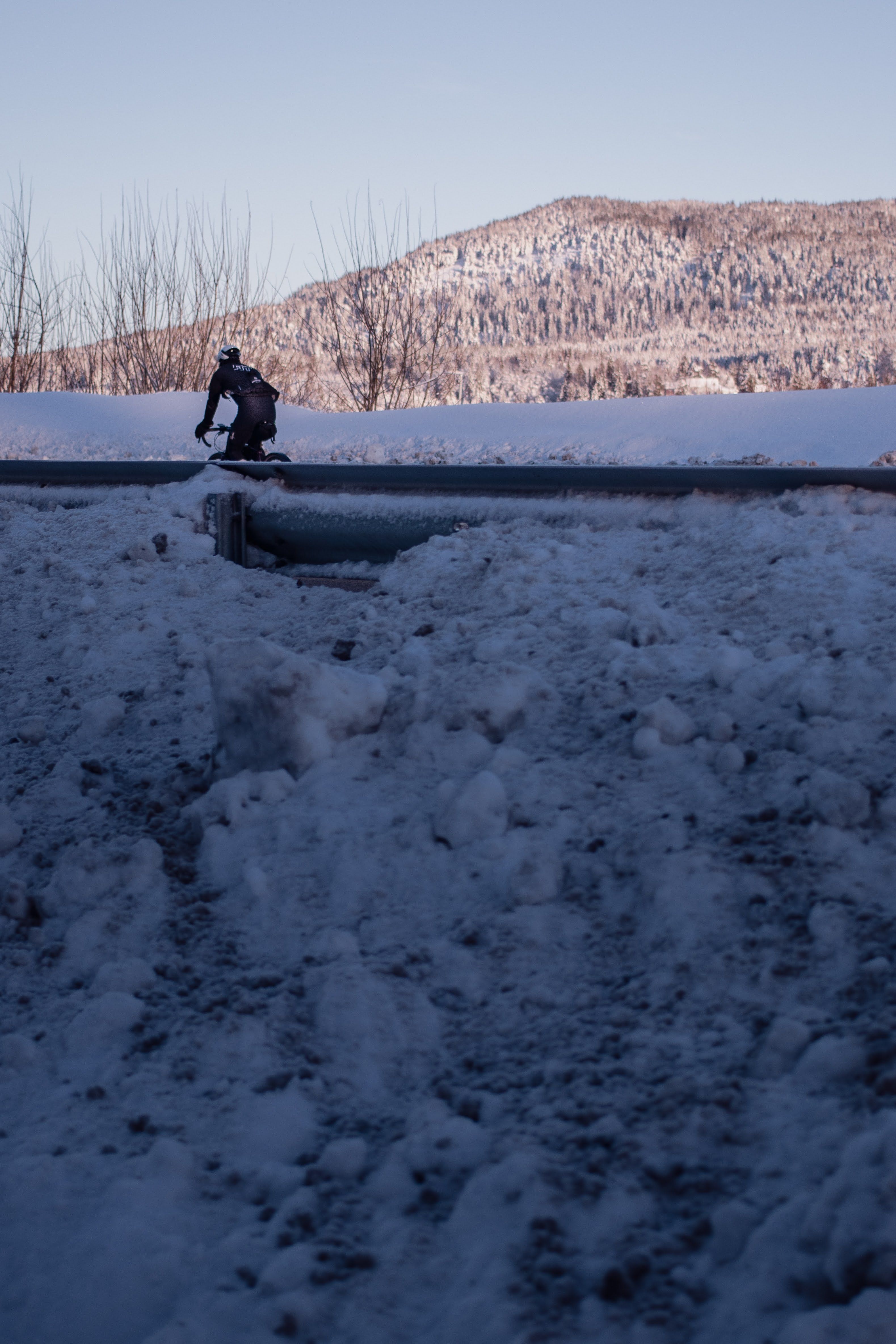 Cyclist in dark winter gear riding through snowy landscape with mountains in background