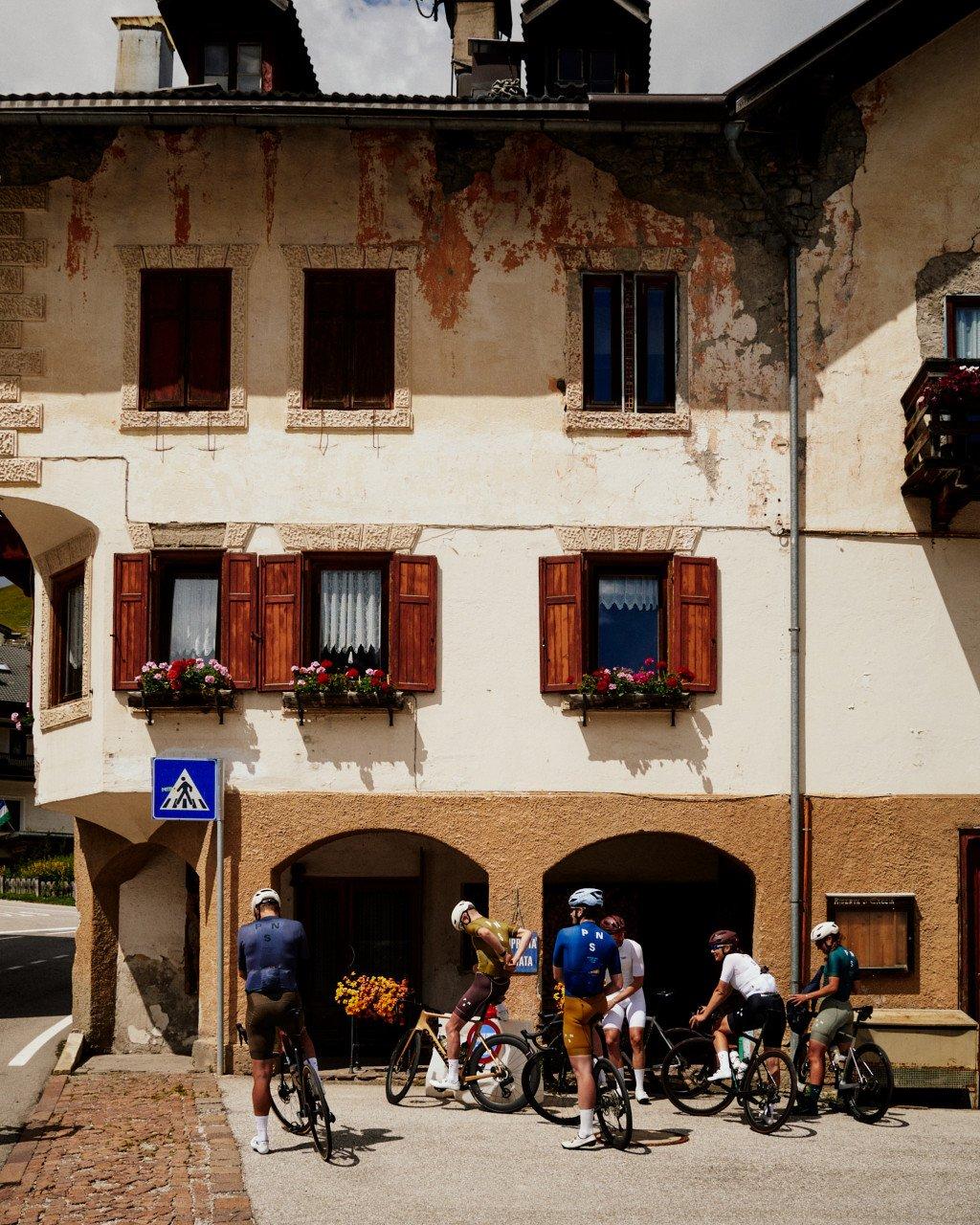 Cyclists gathered with bikes in front of traditional Alpine building with wooden shutters and flower boxes