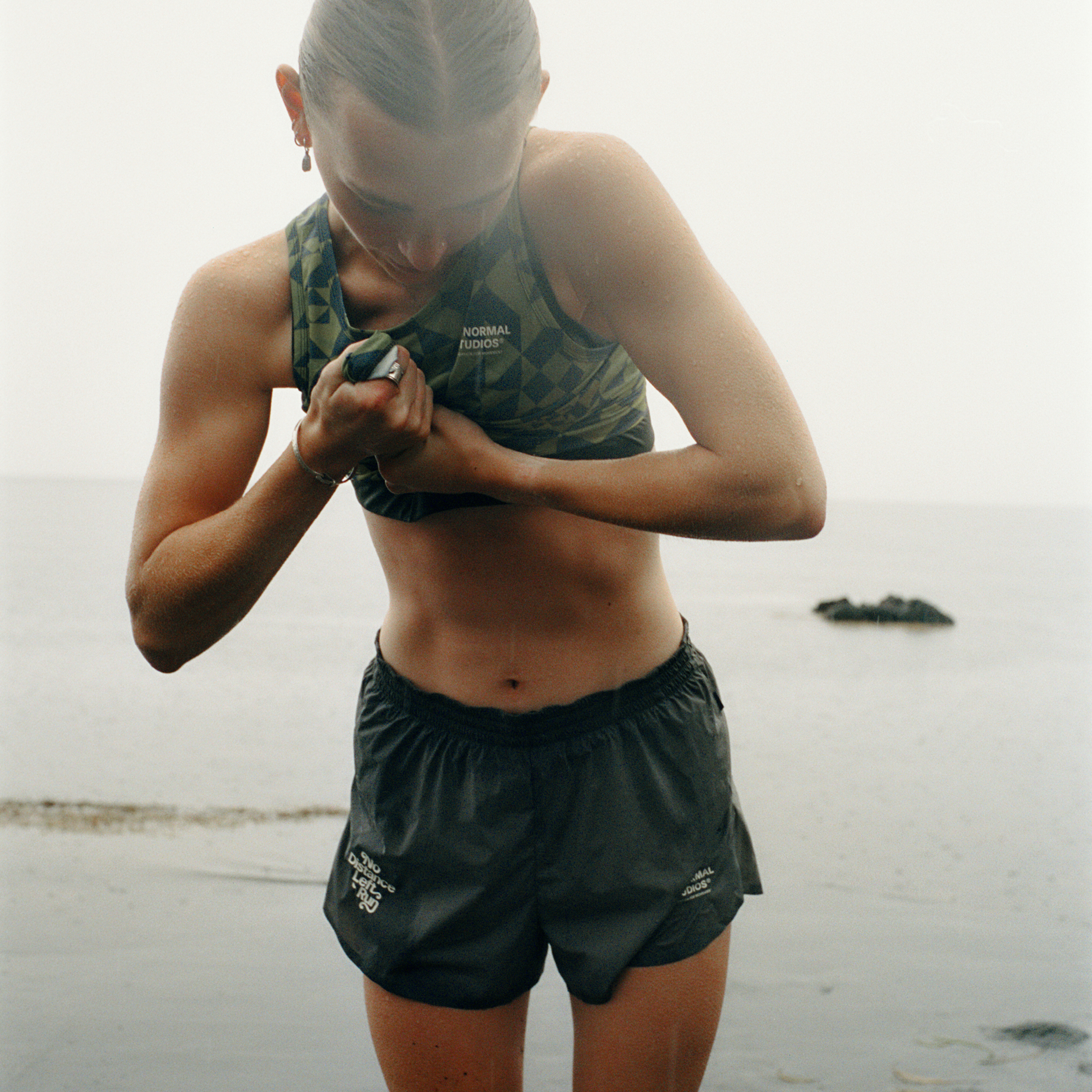 Model wearing green Balance running bra and shorts on beach, adjusting sports watch