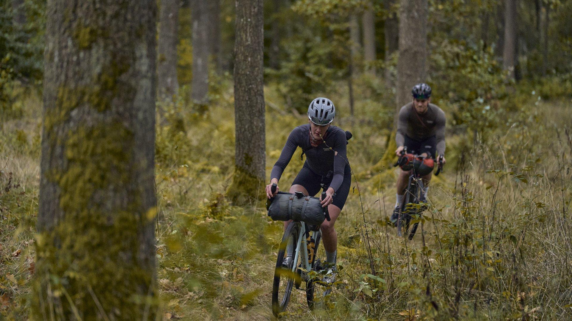 Two cyclists bikepacking through autumn forest wearing dark cycling apparel with frame bags