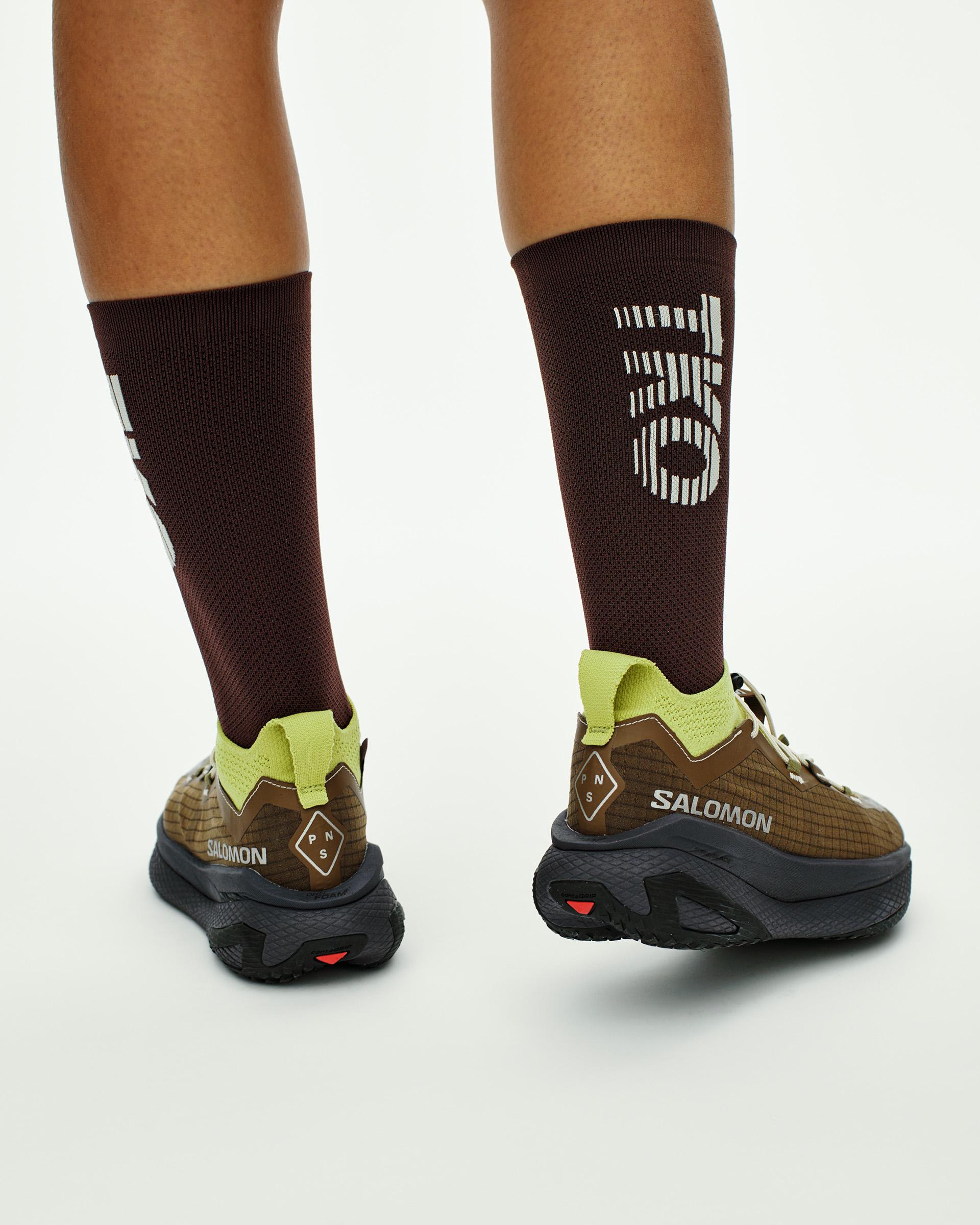 Green Salomon GRVL CONCEPT off-race shoes on model with brown socks showing white PAS logo