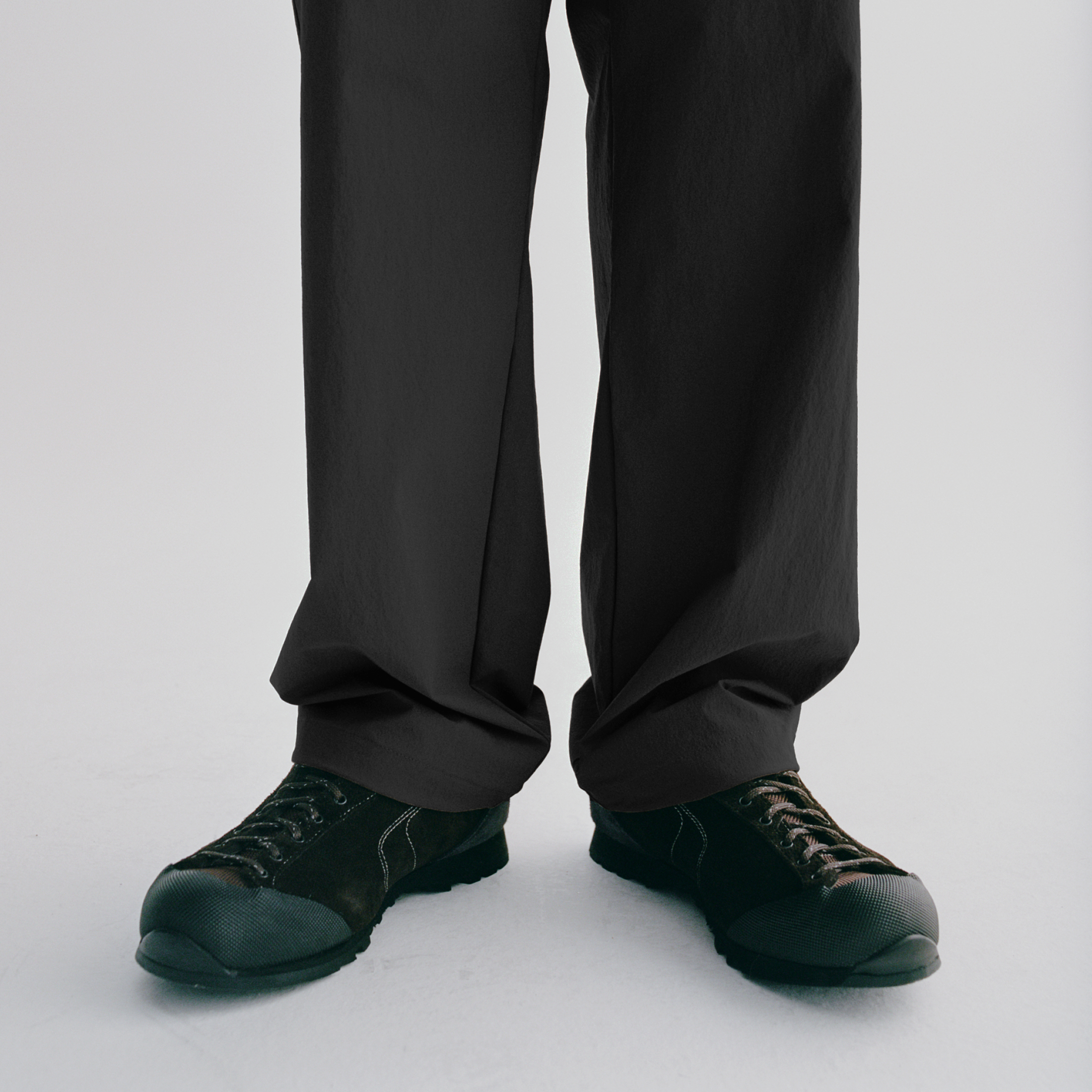 Black trousers with dark green Diemme collaboration sneakers, detail shot of lower legs and feet
