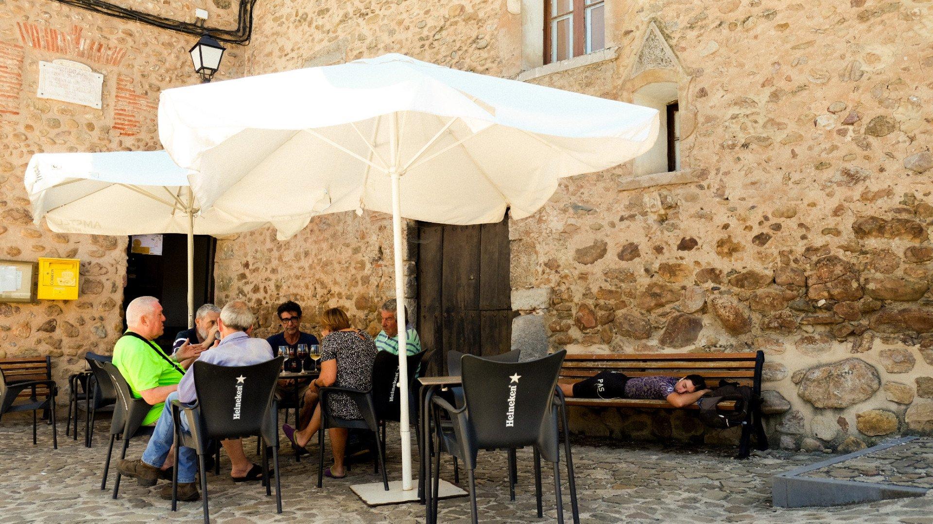 Cyclists resting at outdoor cafe terrace with stone walls and umbrellas
