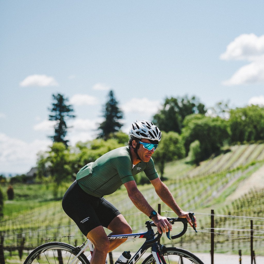 Model wearing green cycling jersey and black bib shorts on time trial bike in Sonoma countryside