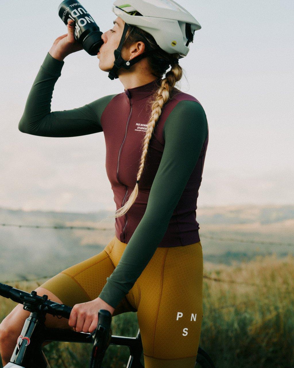 Model wearing colorblocked jersey in burgundy body with green sleeves drinking from water bottle outdoors