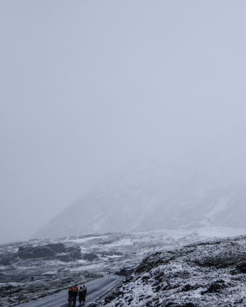 Two cyclists on snowy mountain road in overcast conditions
