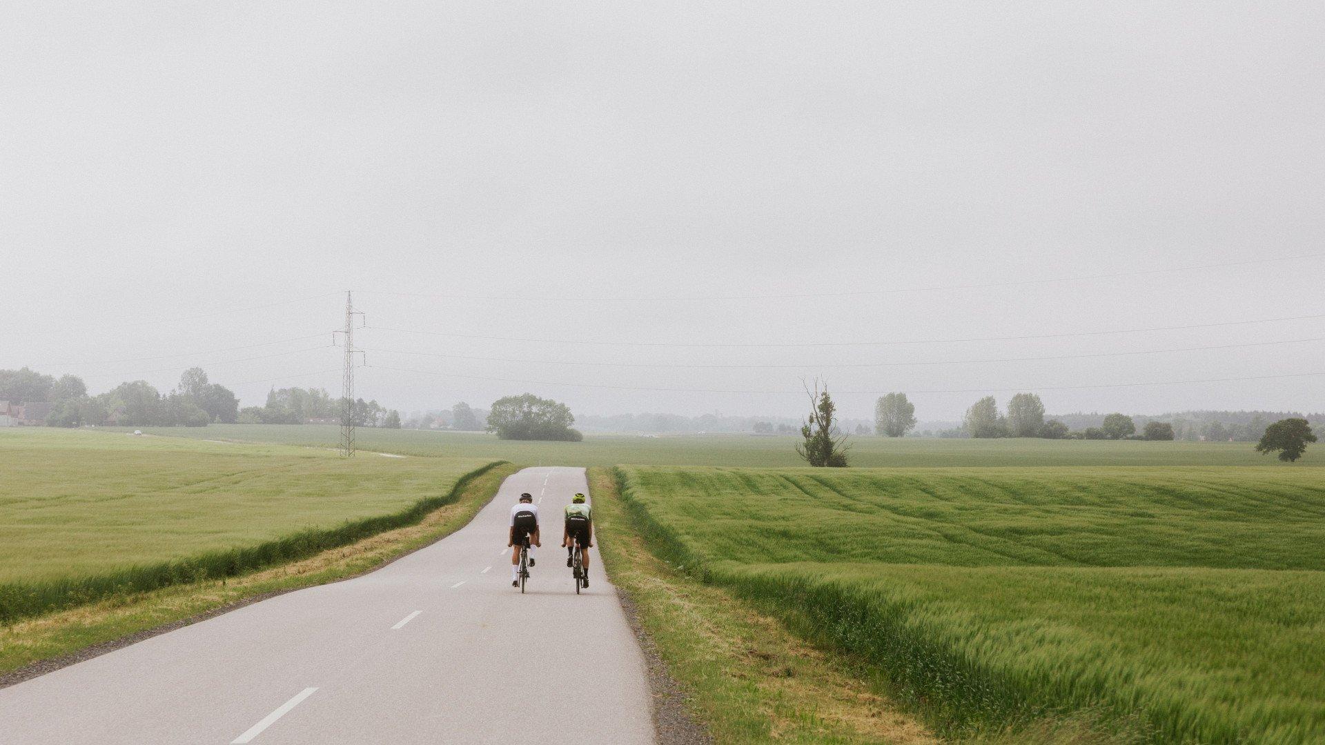 Two cyclists riding on rural road through green countryside fields