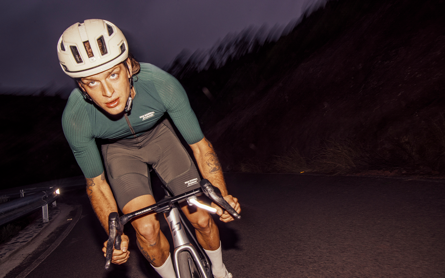Model wearing green Mechanism Pro jersey and brown shorts in aerodynamic position on time trial bike at dusk