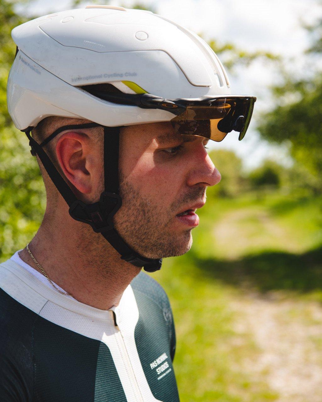Model wearing white aerodynamic time trial helmet with tinted visor in profile view outdoors