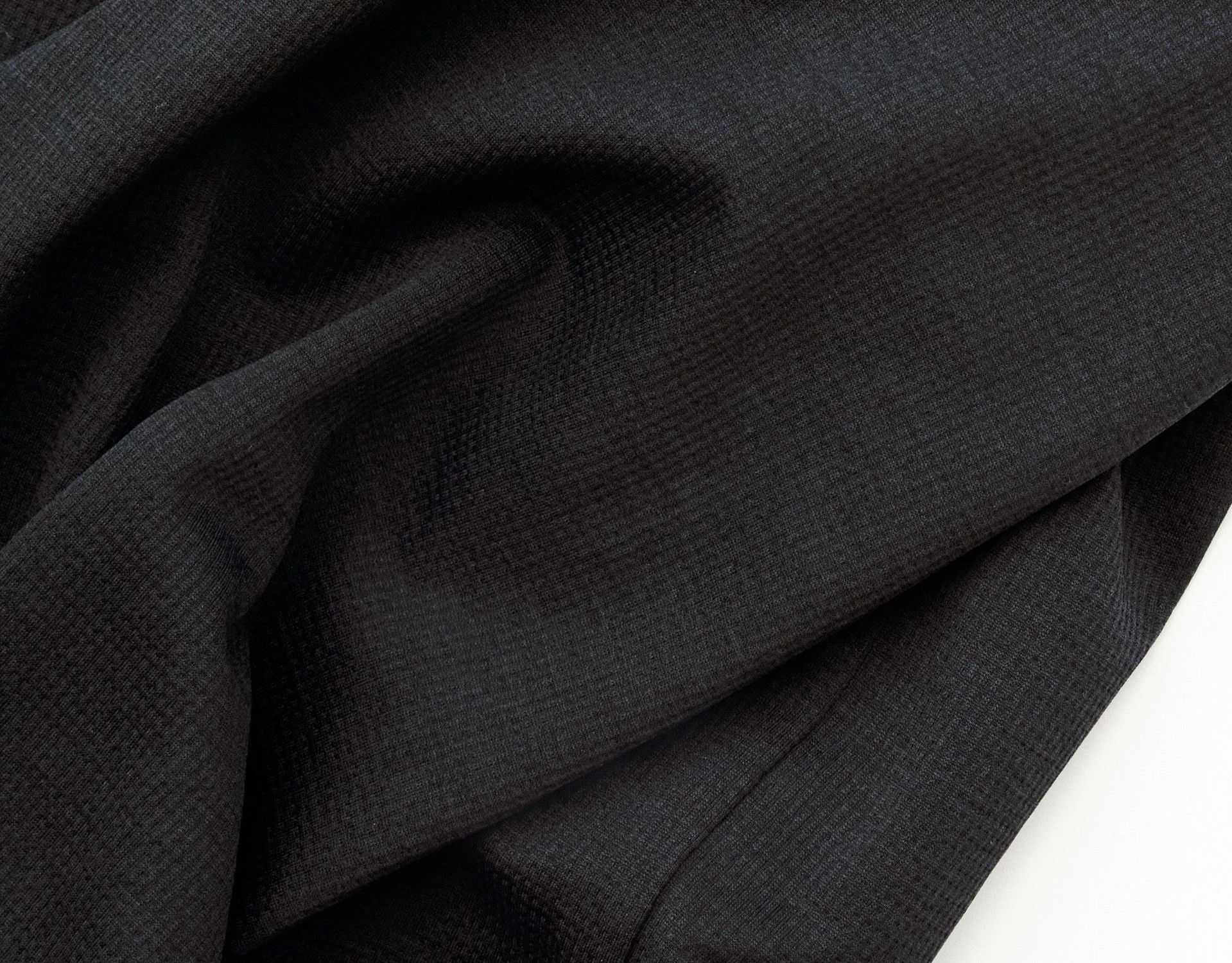 Dark gray lightweight knit fabric with small circular logo detail showing fine textile weave structure