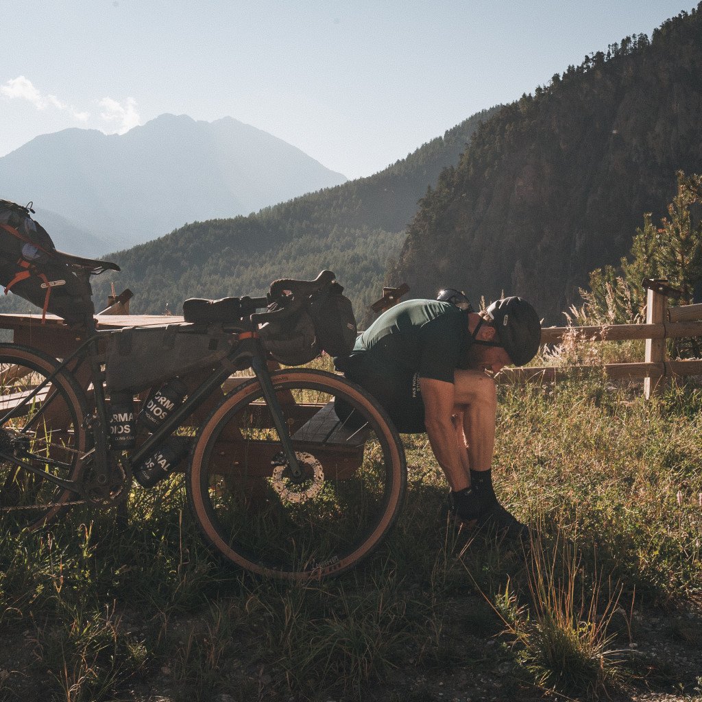 Cyclist in light green jersey examining bikepacking setup in mountain landscape