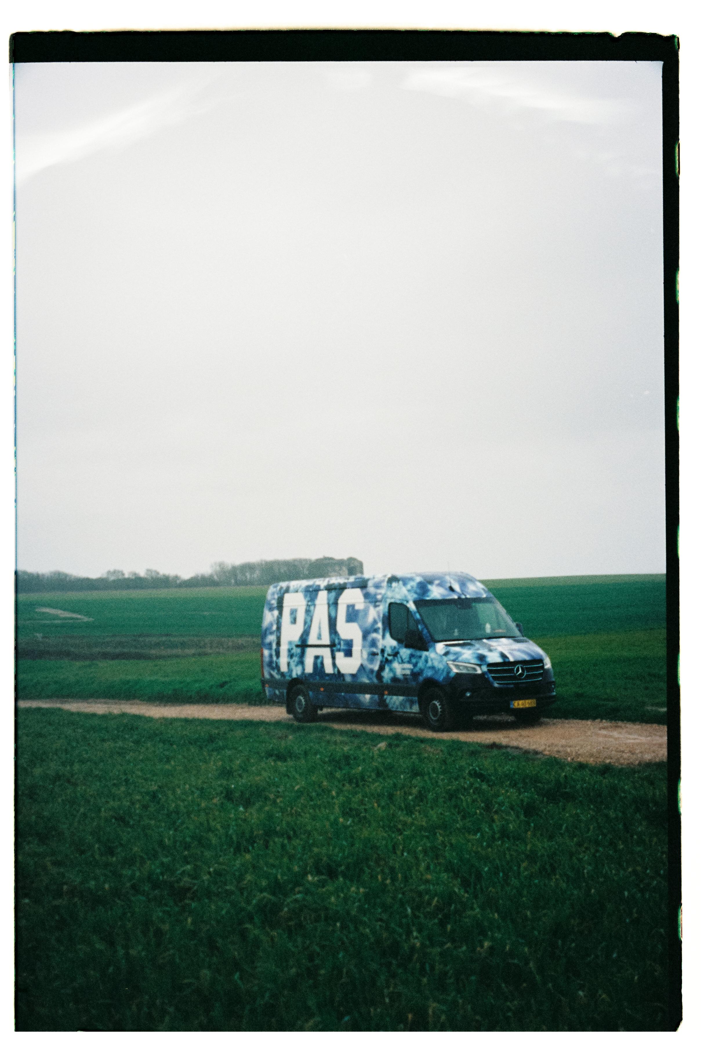 Blue camouflage van with PAS lettering parked in green countryside field