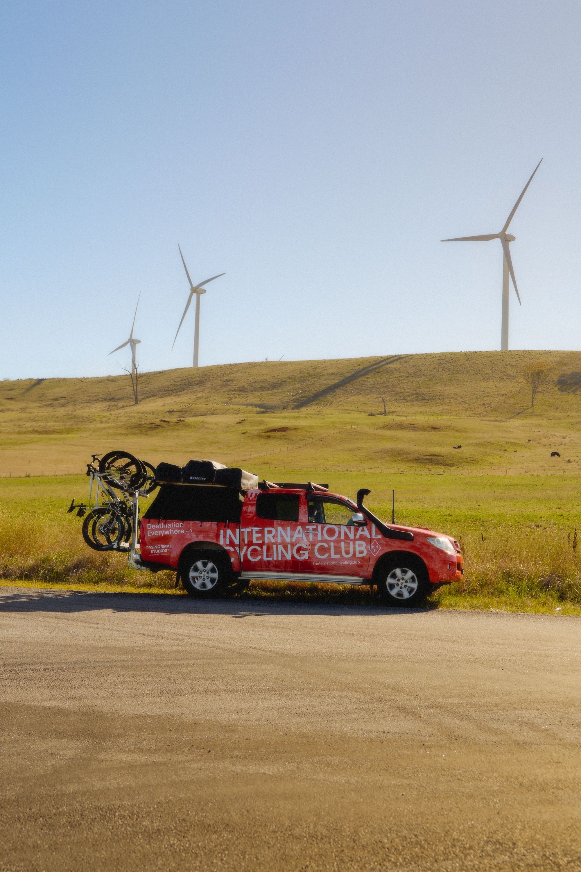 Red pickup truck with bikes on roadside near wind turbines in rural landscape