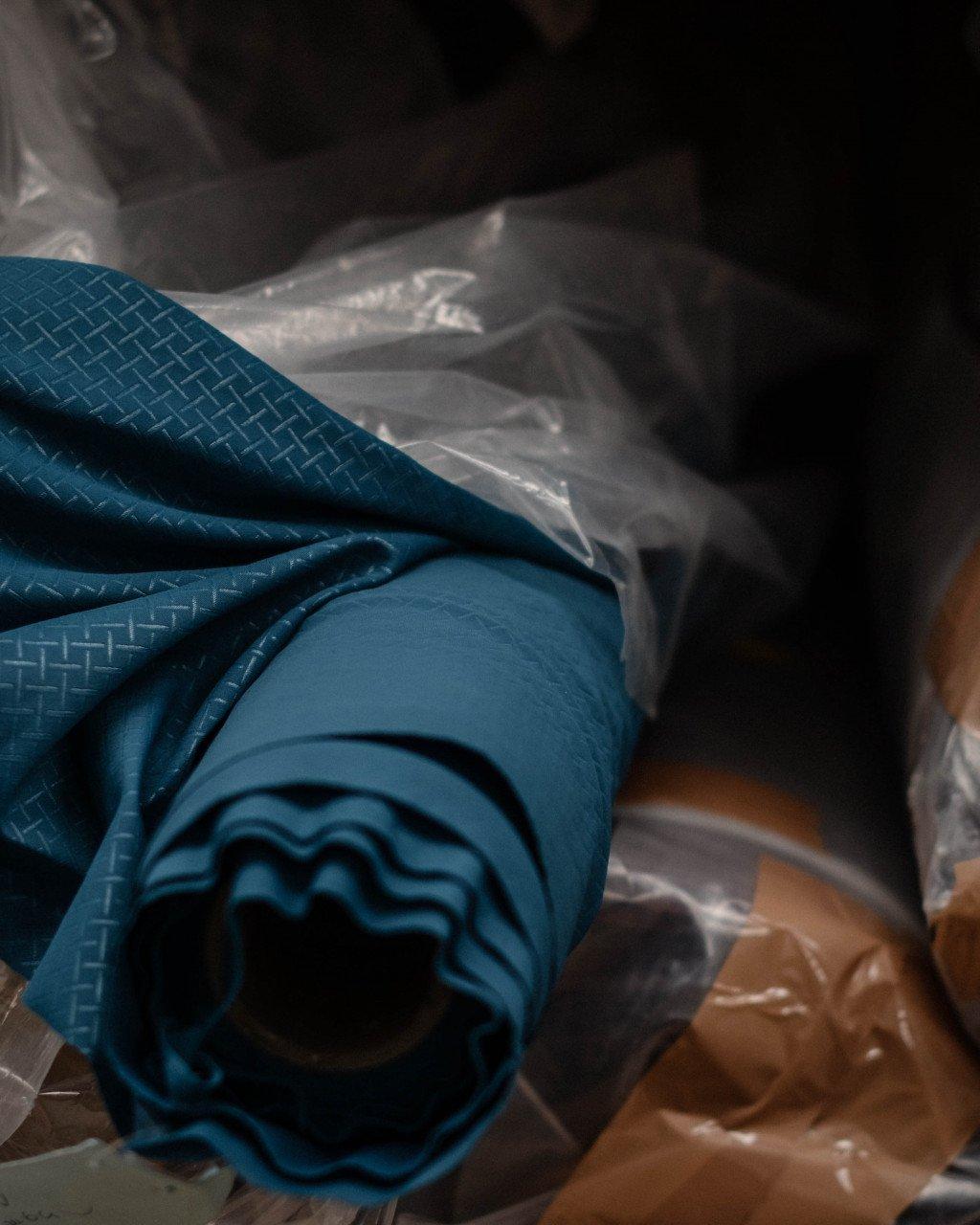 Blue cycling jersey with geometric pattern rolled up in packaging with clear plastic wrap