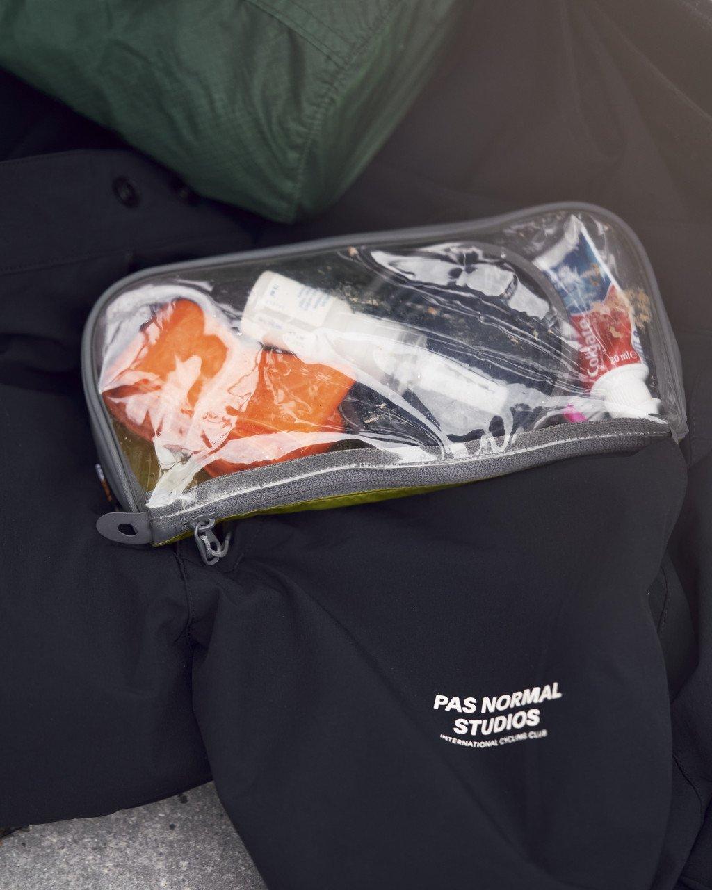Clear toiletry bag with cycling accessories and gear inside, resting on black bag with logo
