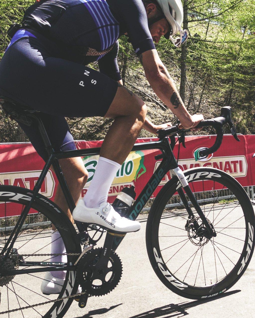 Model wearing black cycling kit with purple details racing on road bike during Giro d'Italia