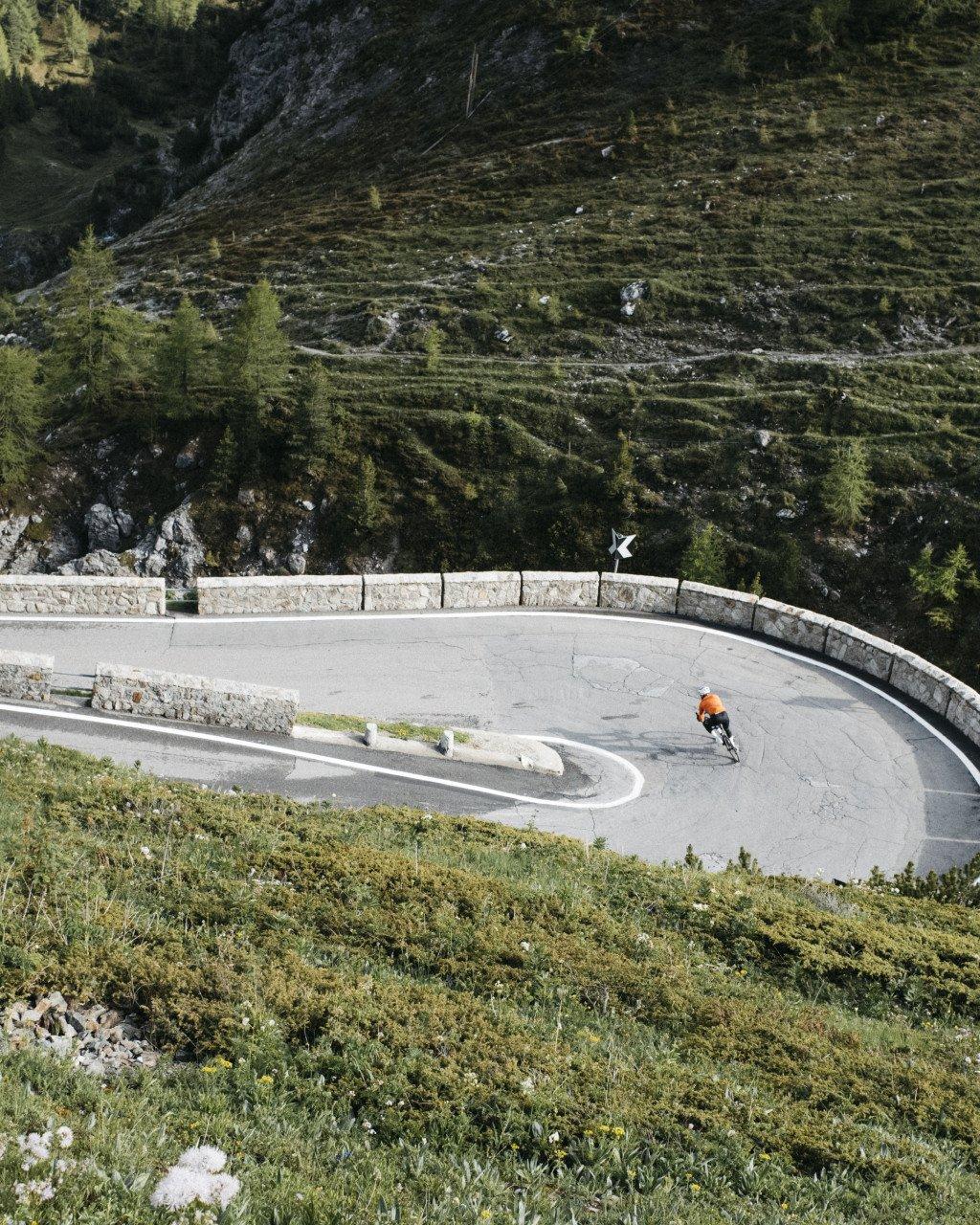Cyclist in orange jersey navigating mountain hairpin turn on alpine road