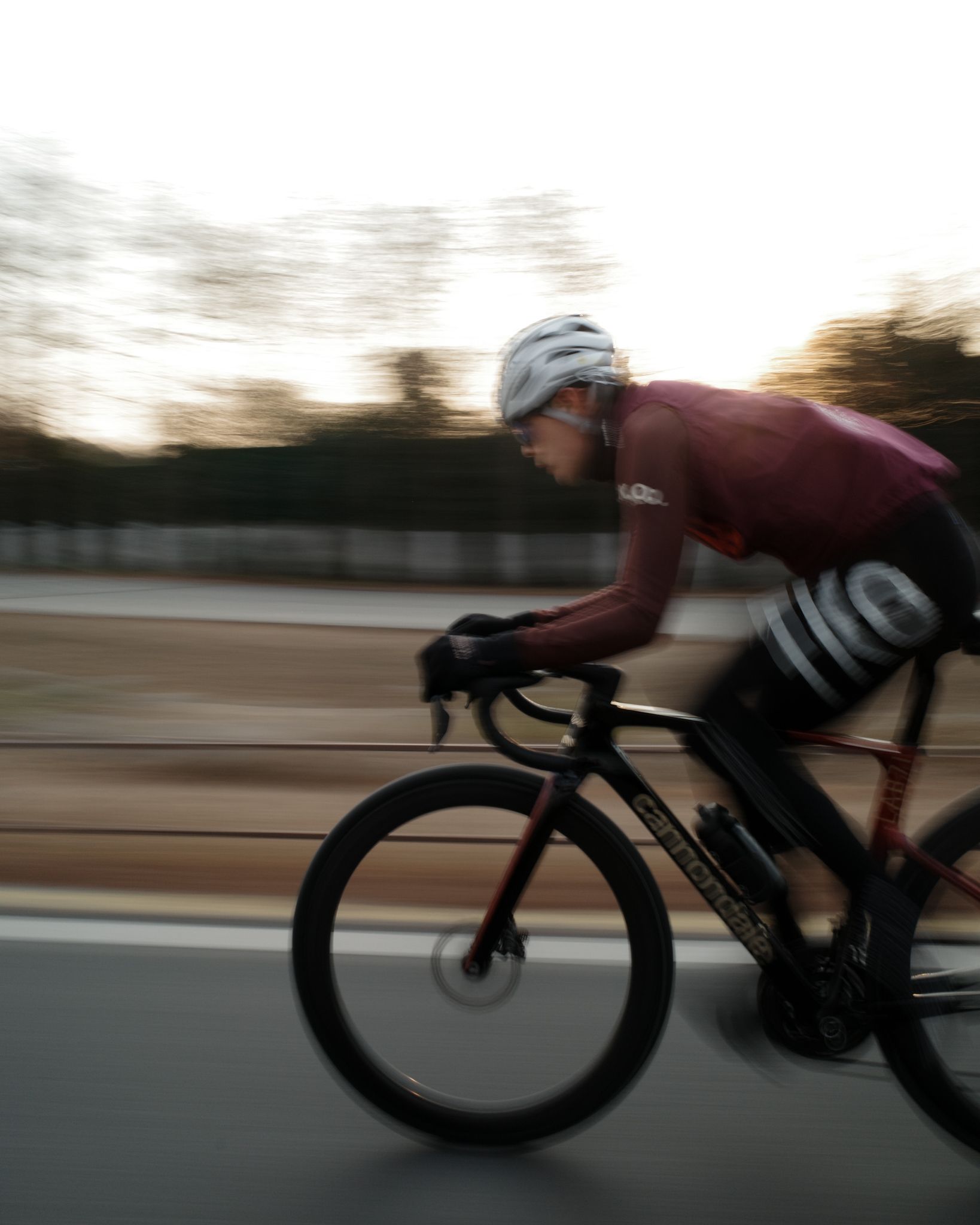 Model wearing burgundy long-sleeve jersey cycling in aerodynamic position with motion blur