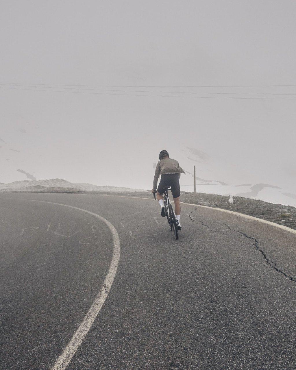 Model wearing grey top and dark shorts cycling on mountain road in misty conditions