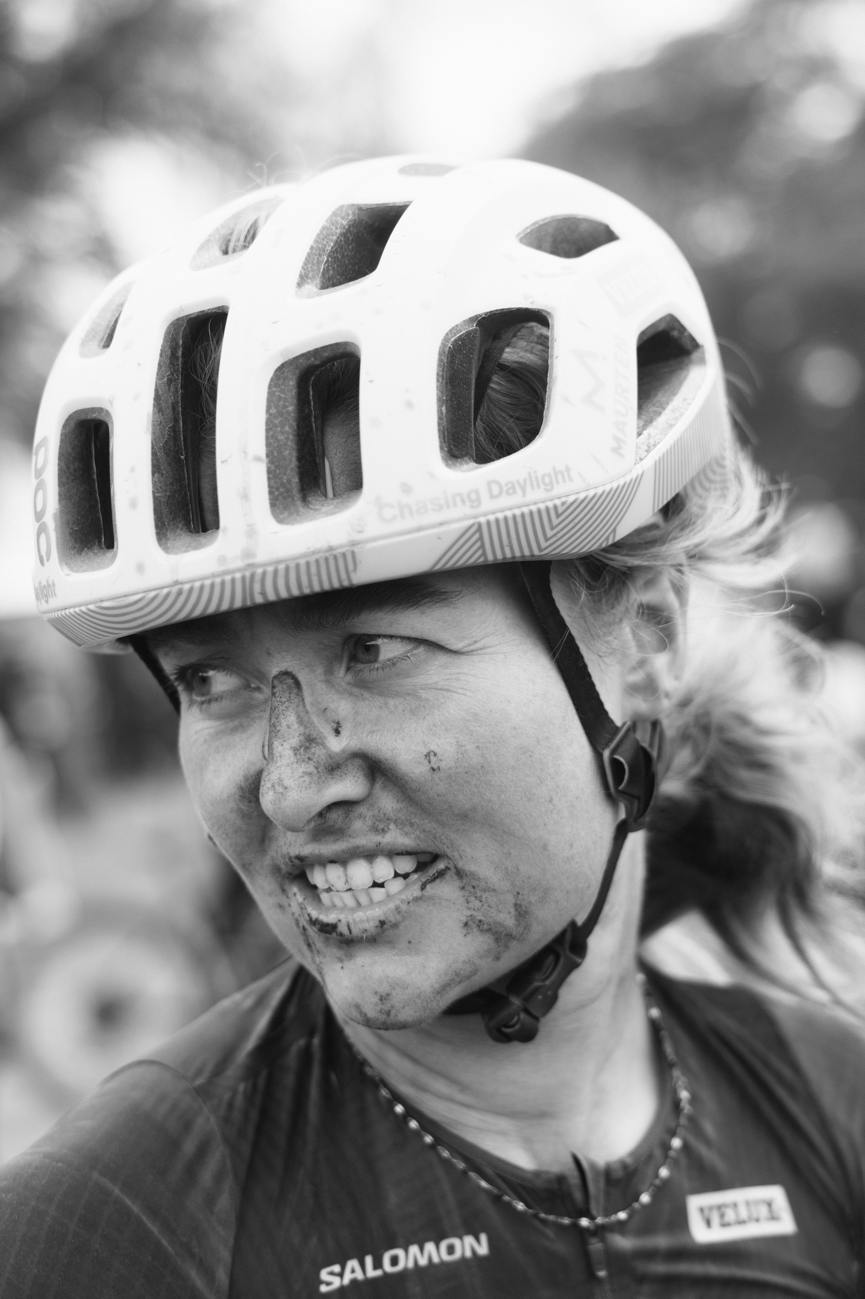 Female cyclist wearing white helmet smiling with dirt on face after gravel race