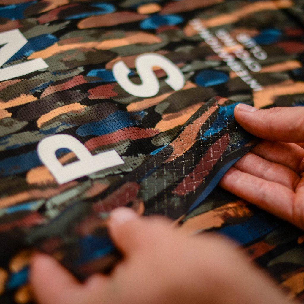 Hands examining camo print cycling jersey fabric with logo lettering detail
