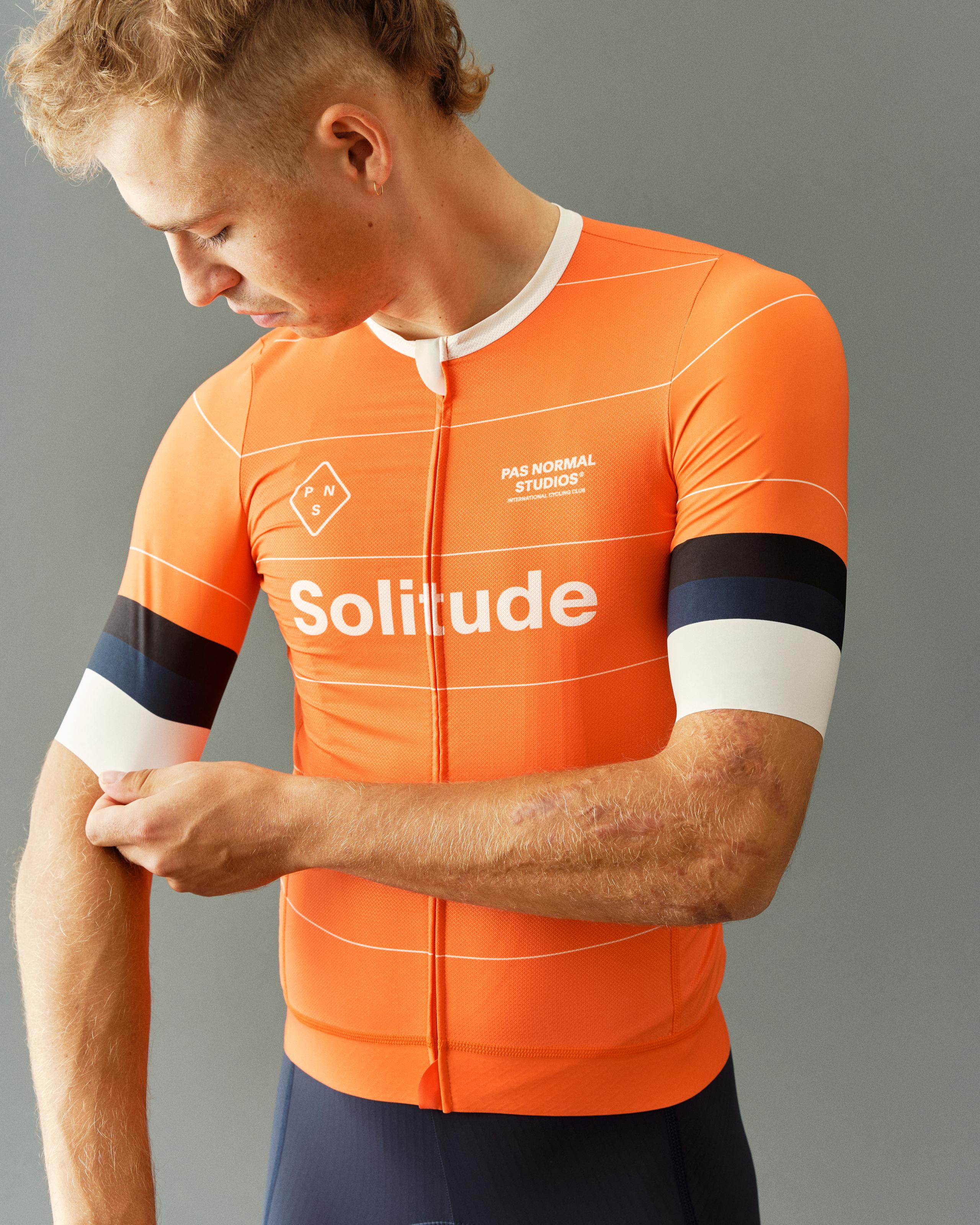 Model wearing Men's Solitude Jersey in bright orange with white and dark blue sleeve stripes and chest branding