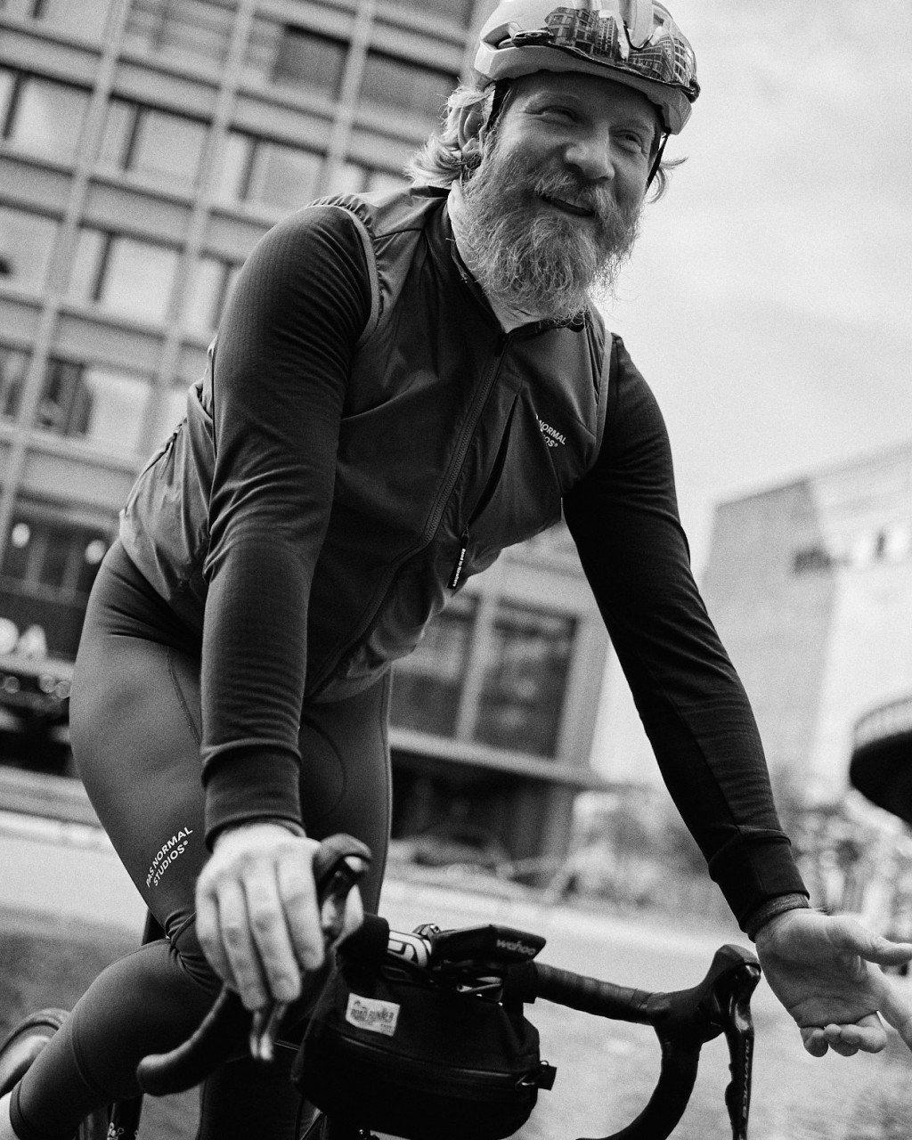 Model wearing dark cycling jersey with logo branding on bike in urban setting