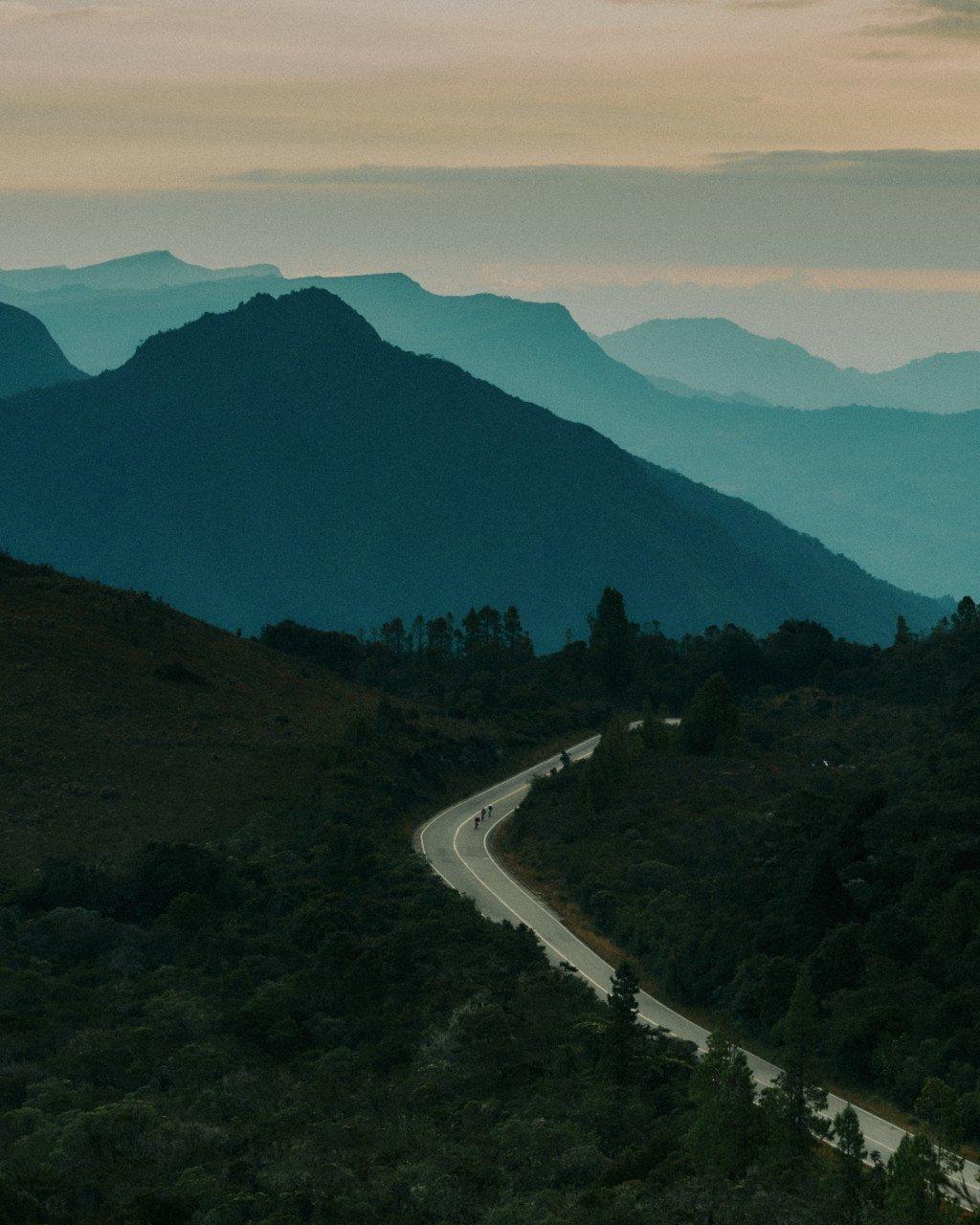 Winding mountain road through layered hills at dusk with cyclists