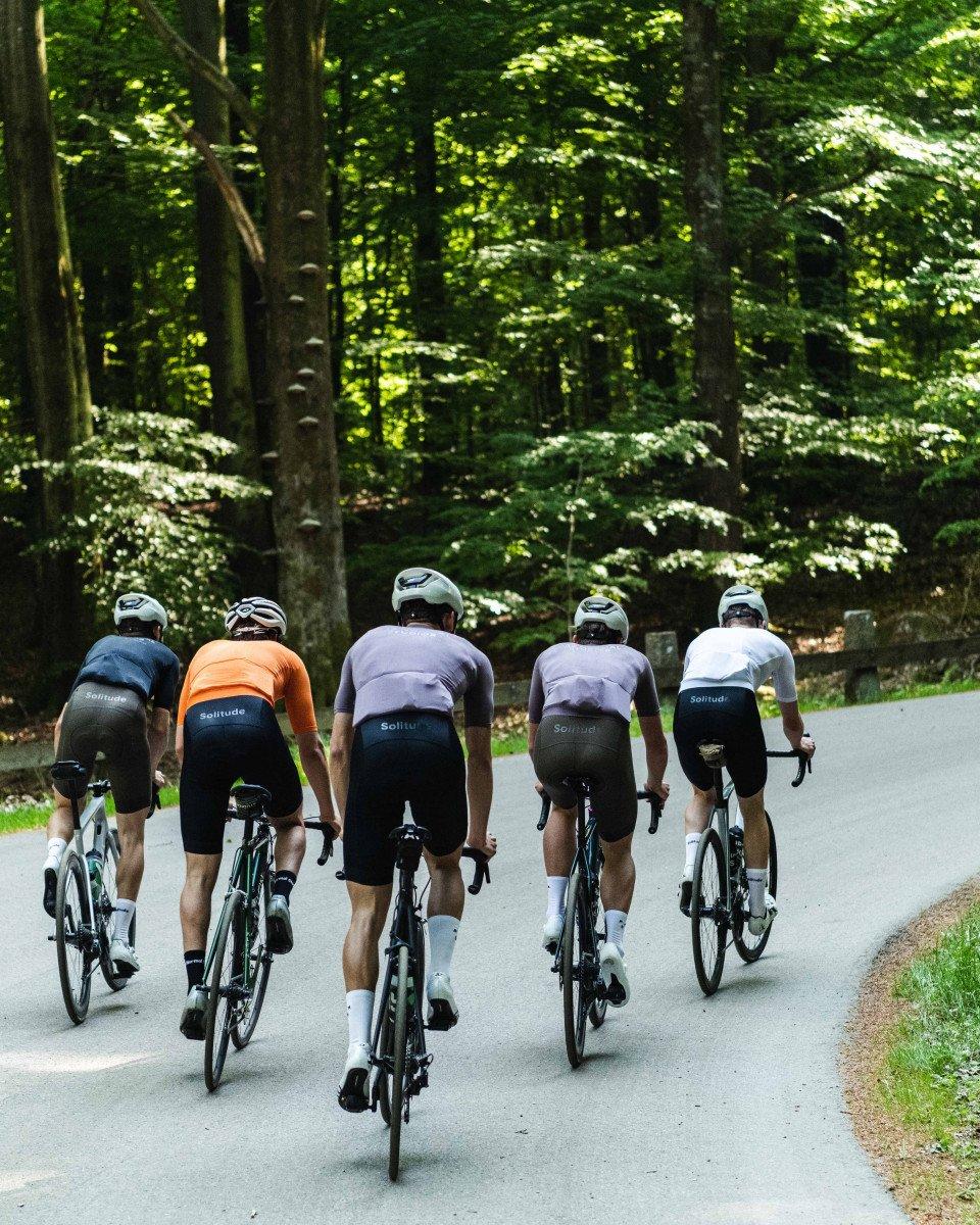 Five cyclists riding together on forest road wearing colorful jerseys and matching black shorts