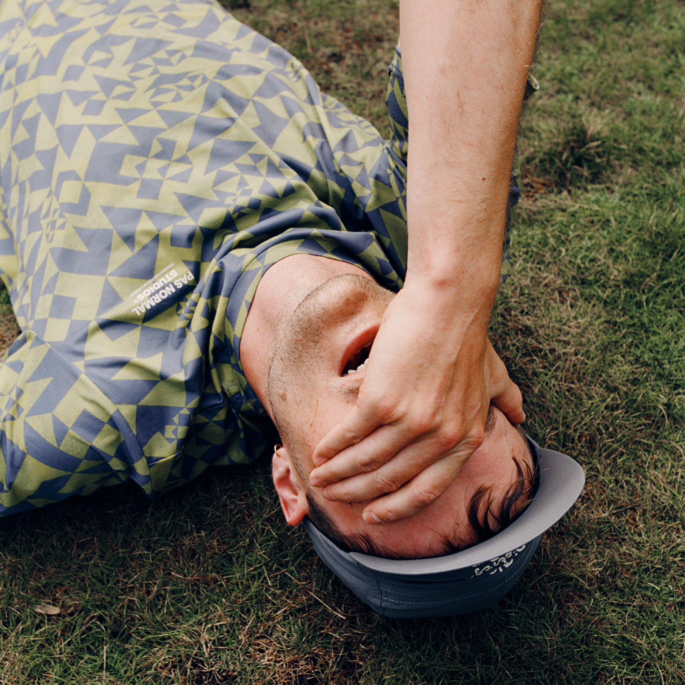 Model wearing green and grey geometric print jersey lying on grass with hand covering face