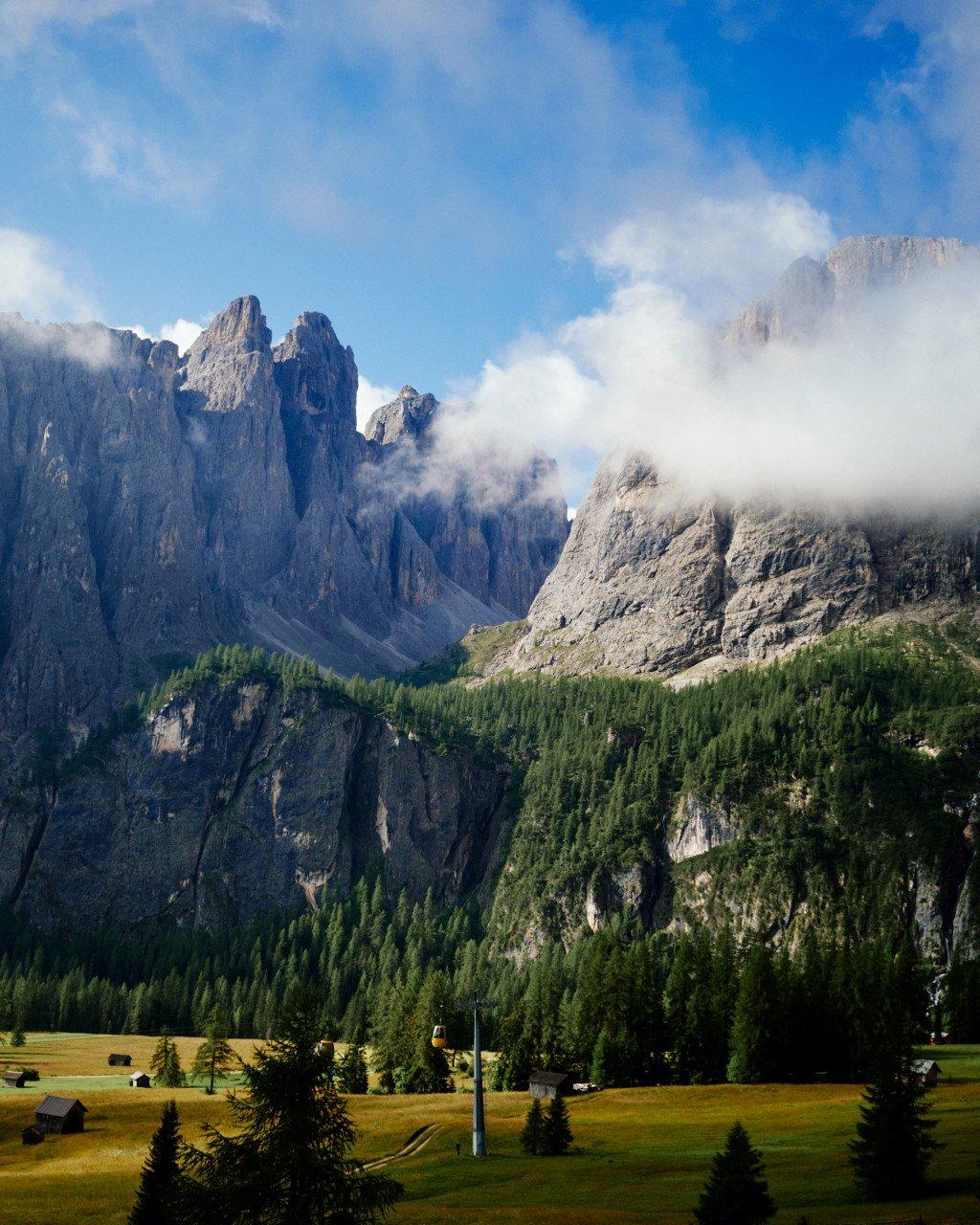 Alpine mountain landscape with dramatic peaks and forest-covered slopes under cloudy sky