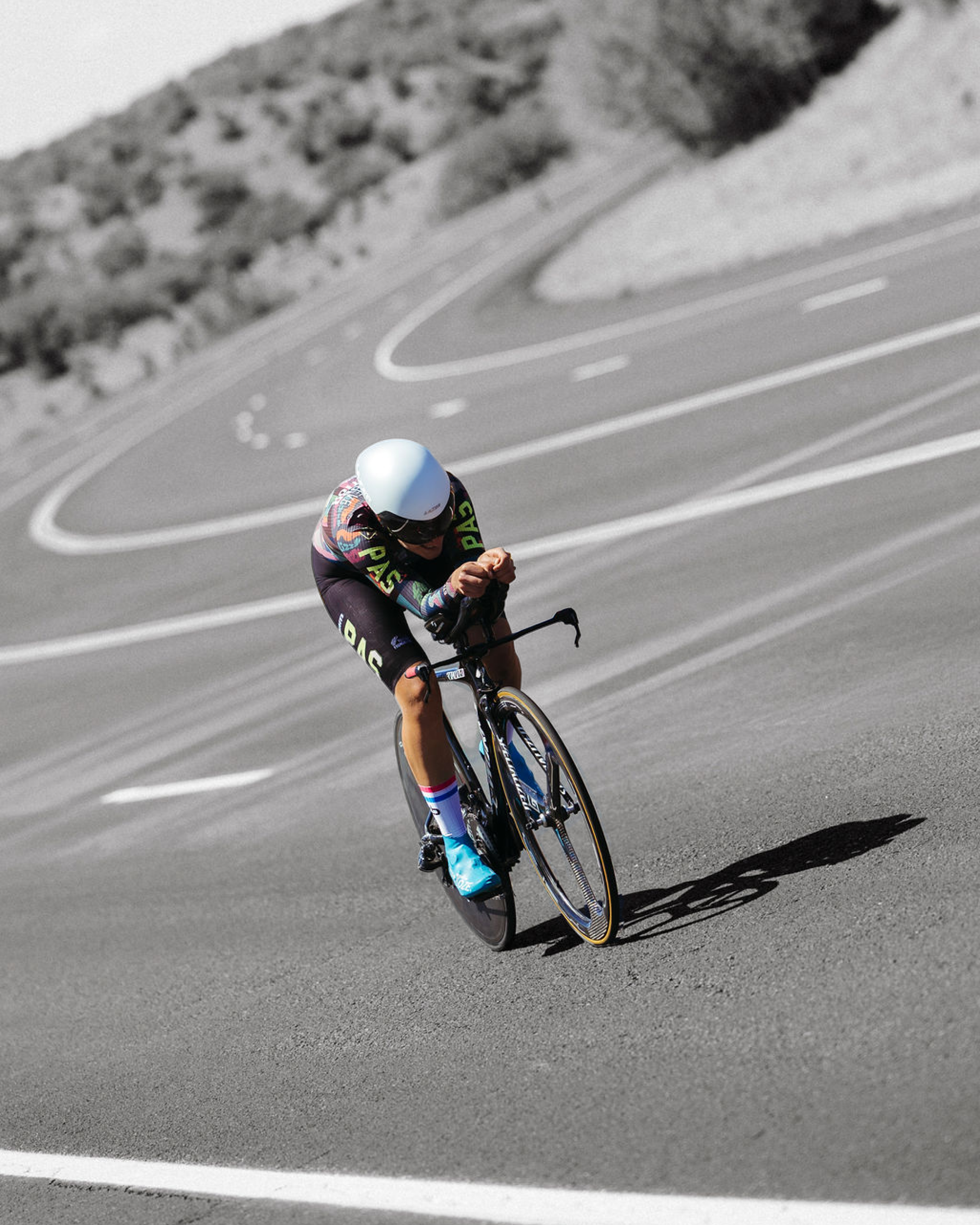 Model wearing black skinsuit with colorful graphics in aerodynamic position on time trial bike on road course