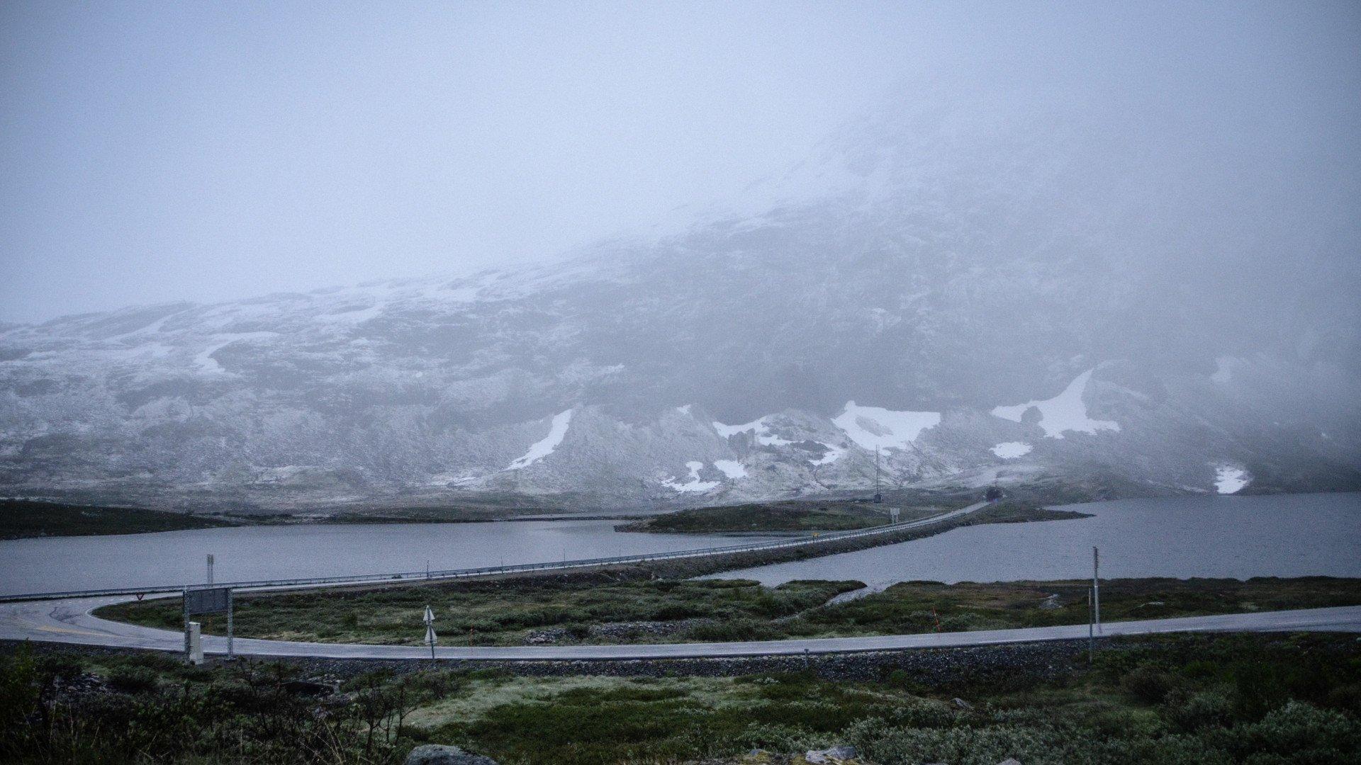 Misty Norwegian landscape with winding coastal road and snow-capped mountains