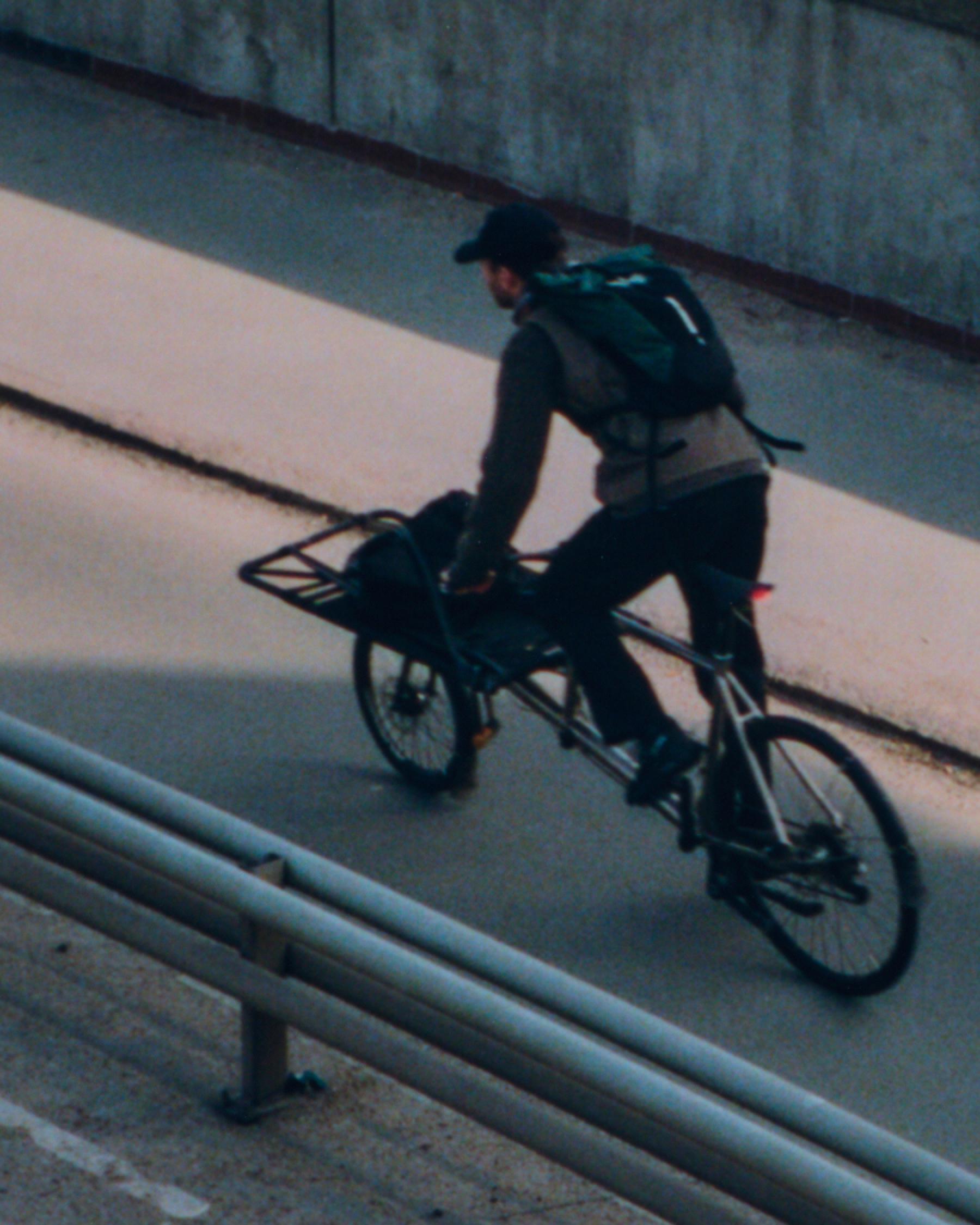 Model wearing dark cycling outfit riding bike through concrete underpass with front basket