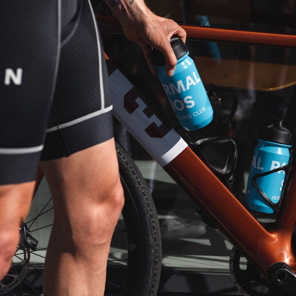 Hand reaching for blue cycling water bottle from bike frame with logo branding visible